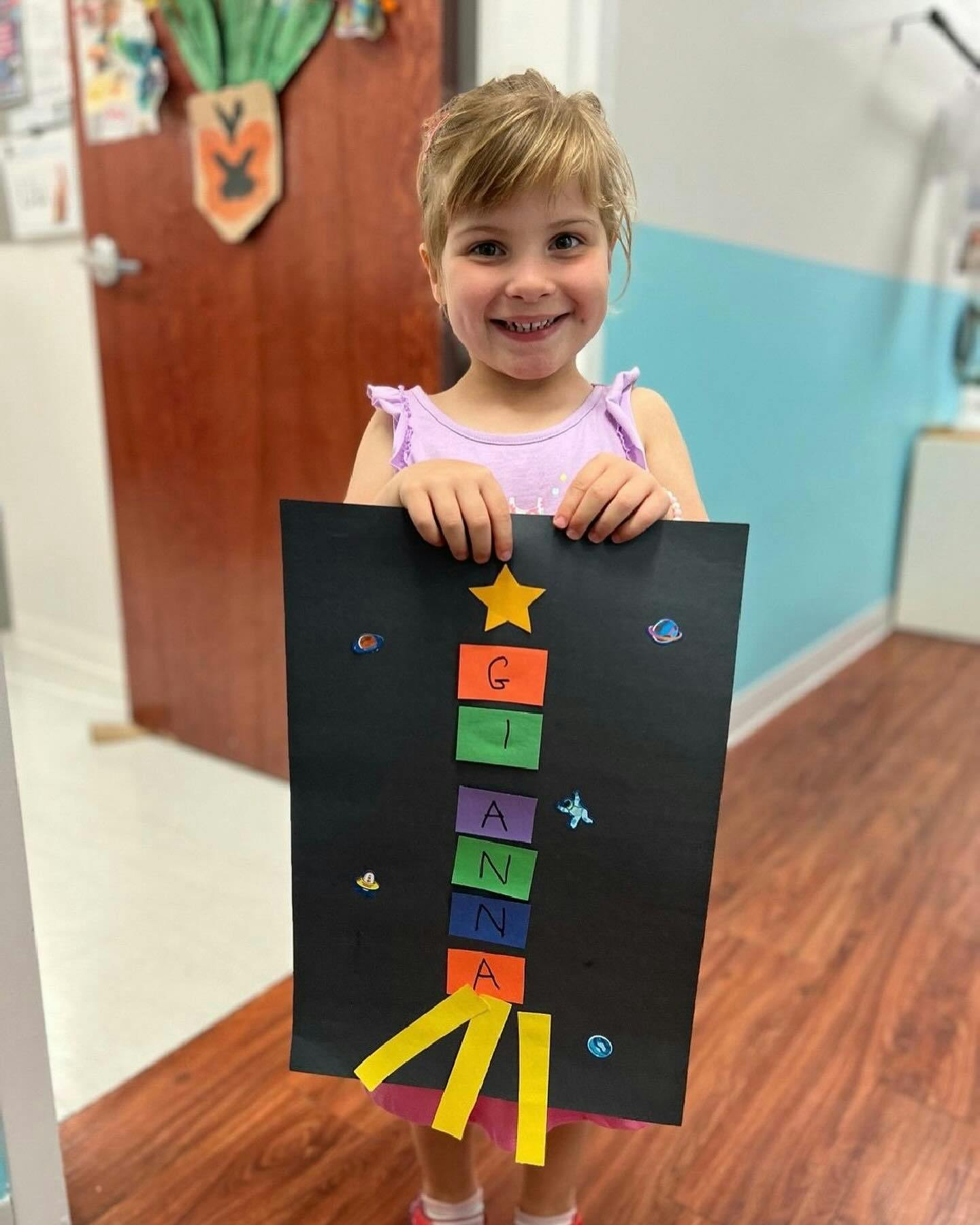 Child holding a black poster board with colorful letters spelling GIANNA