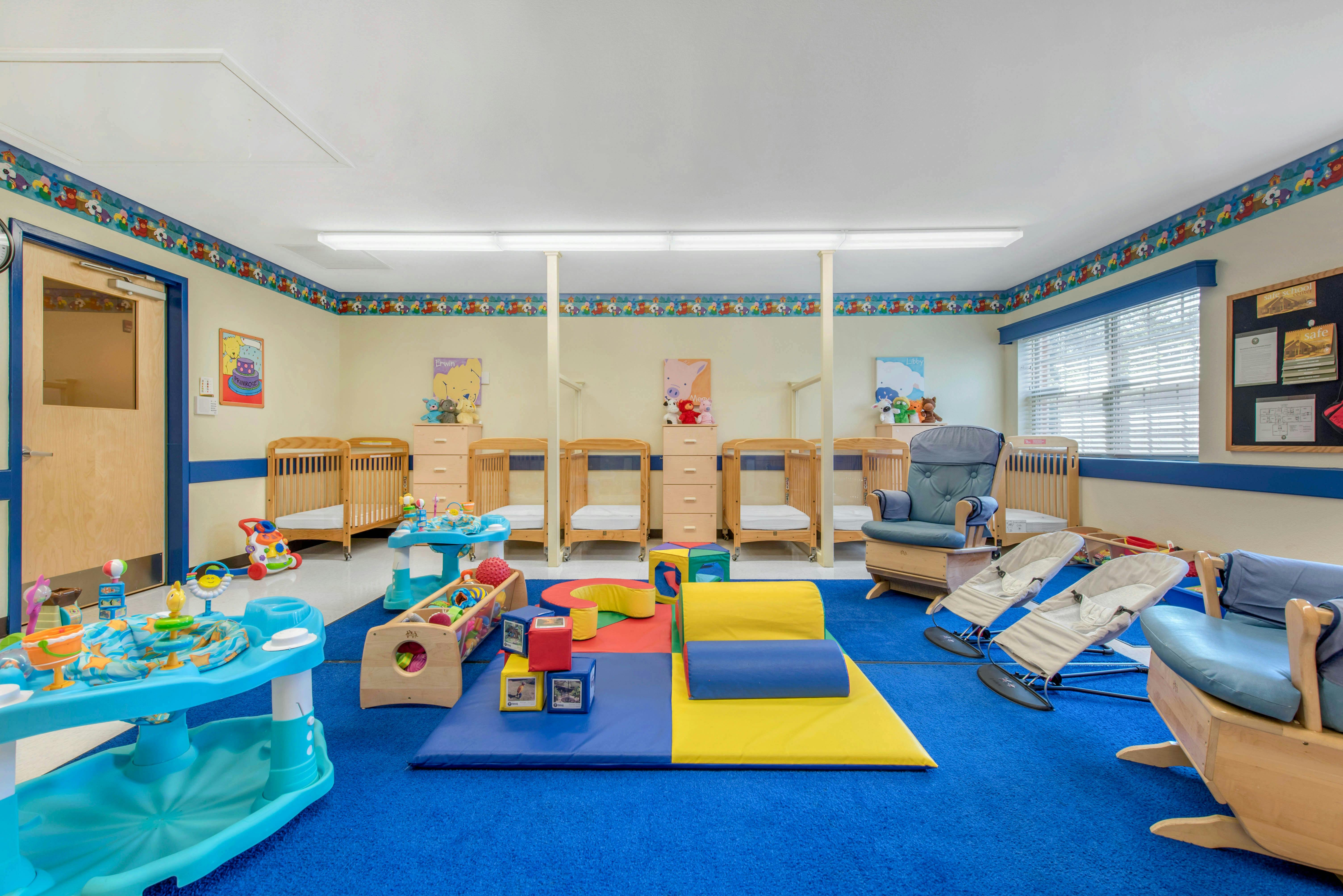 A colorful childcare room with cribs, play mats, and baby gear