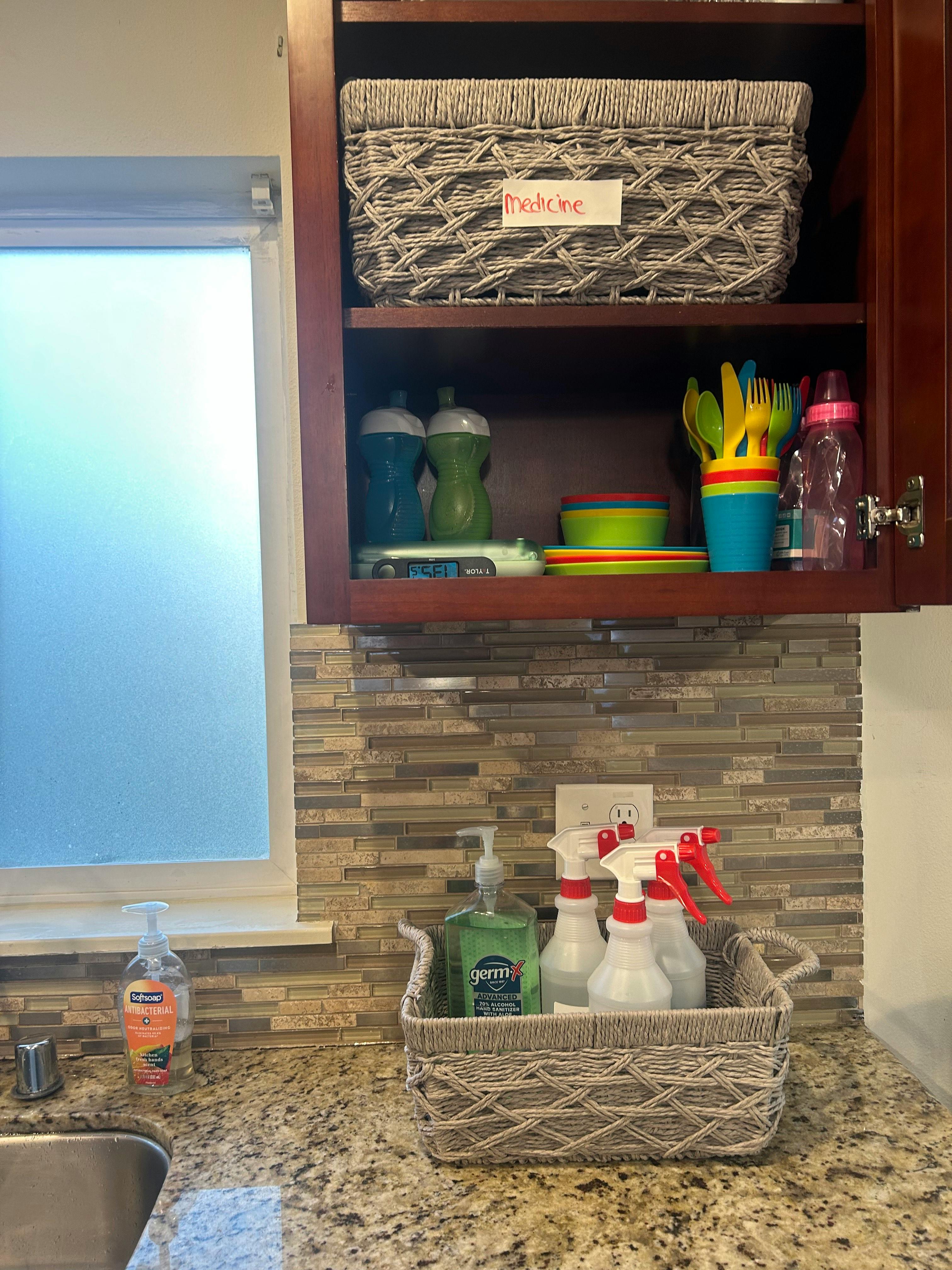 Kitchen counter with cleaning supplies in a basket and cabinet with children's dishes