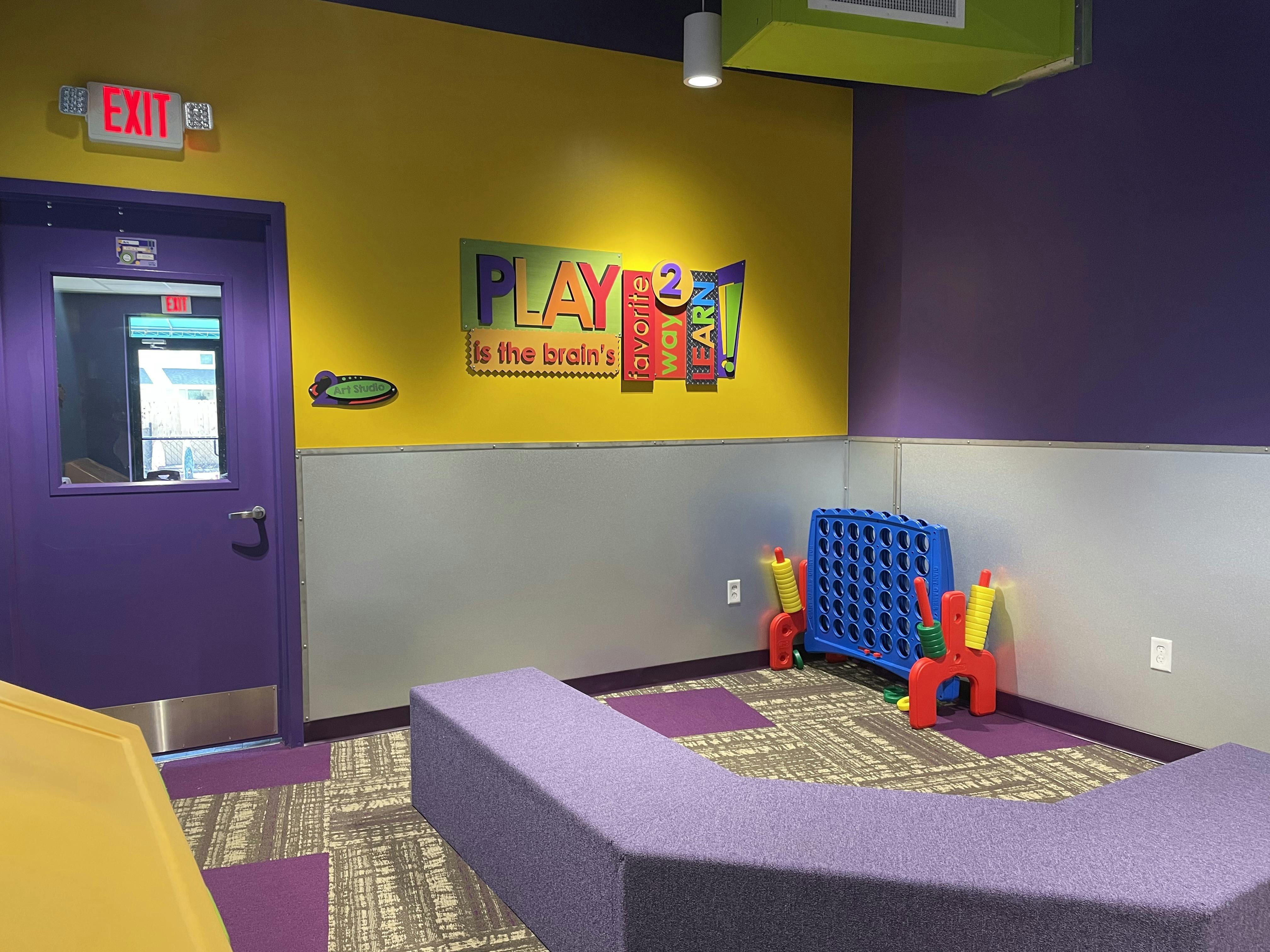 Room with yellow and purple walls, "PLAY is the brain's favorite way 2 LEARN" sign