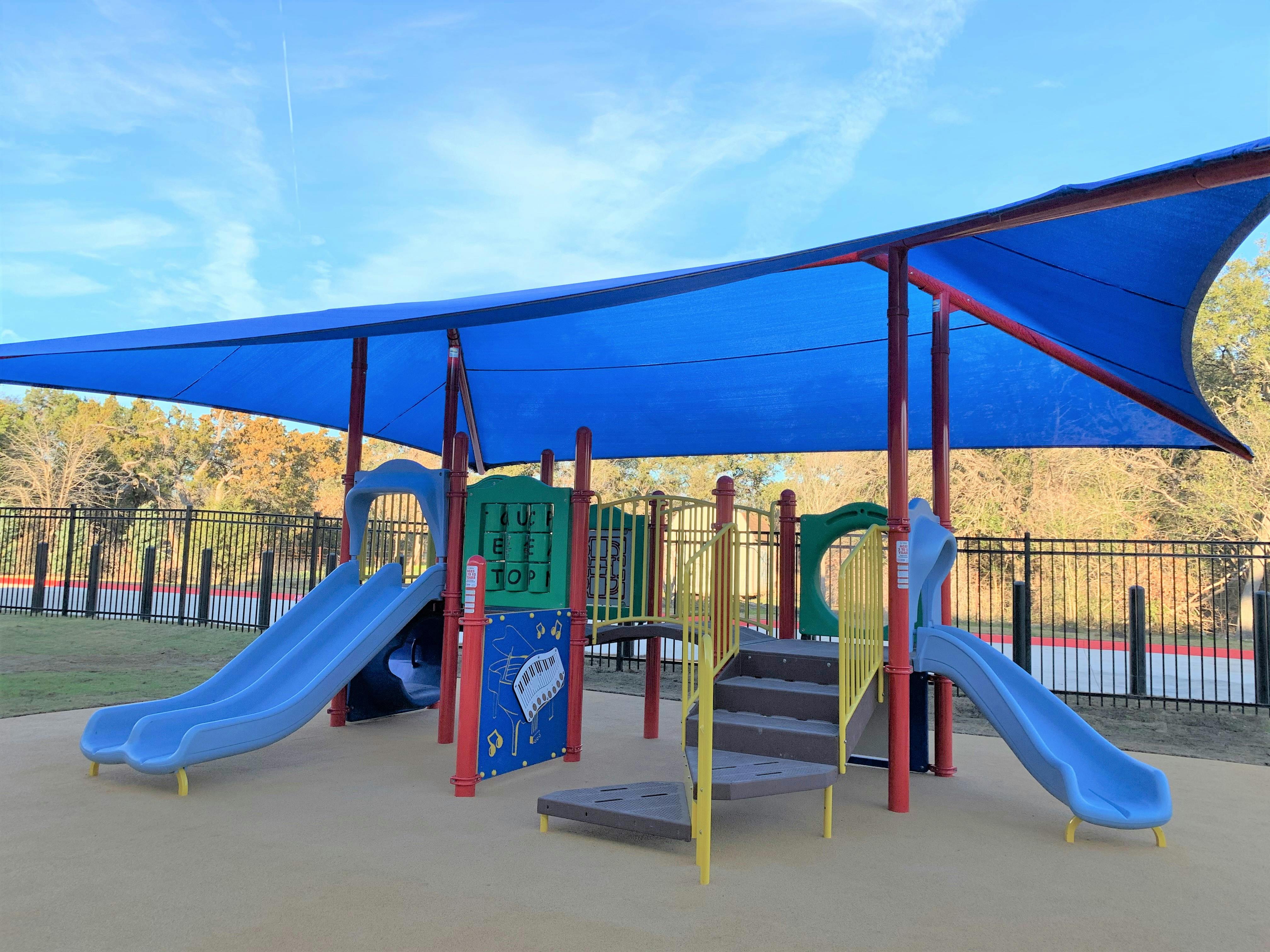 Playground with slides and climbing structures under a blue shade canopy