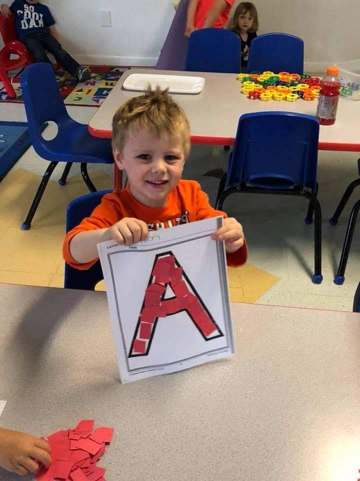 Child holding up a paper with a red letter A on it
