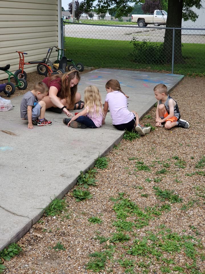 Adult and three children sitting on concrete, one child sitting on gravel
