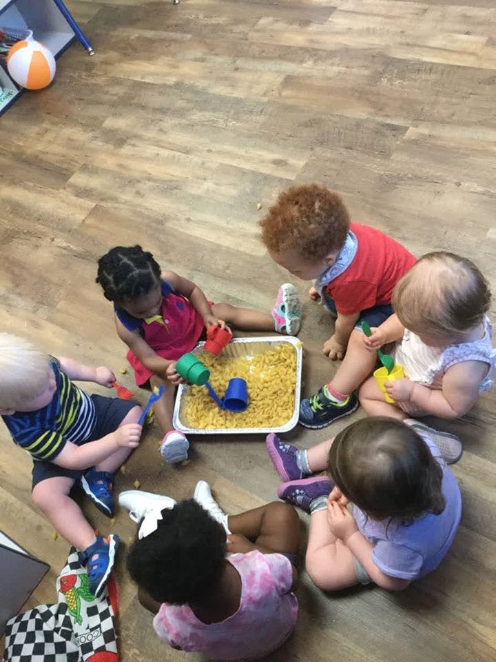 Children playing with pasta and toys in a tray on the floor