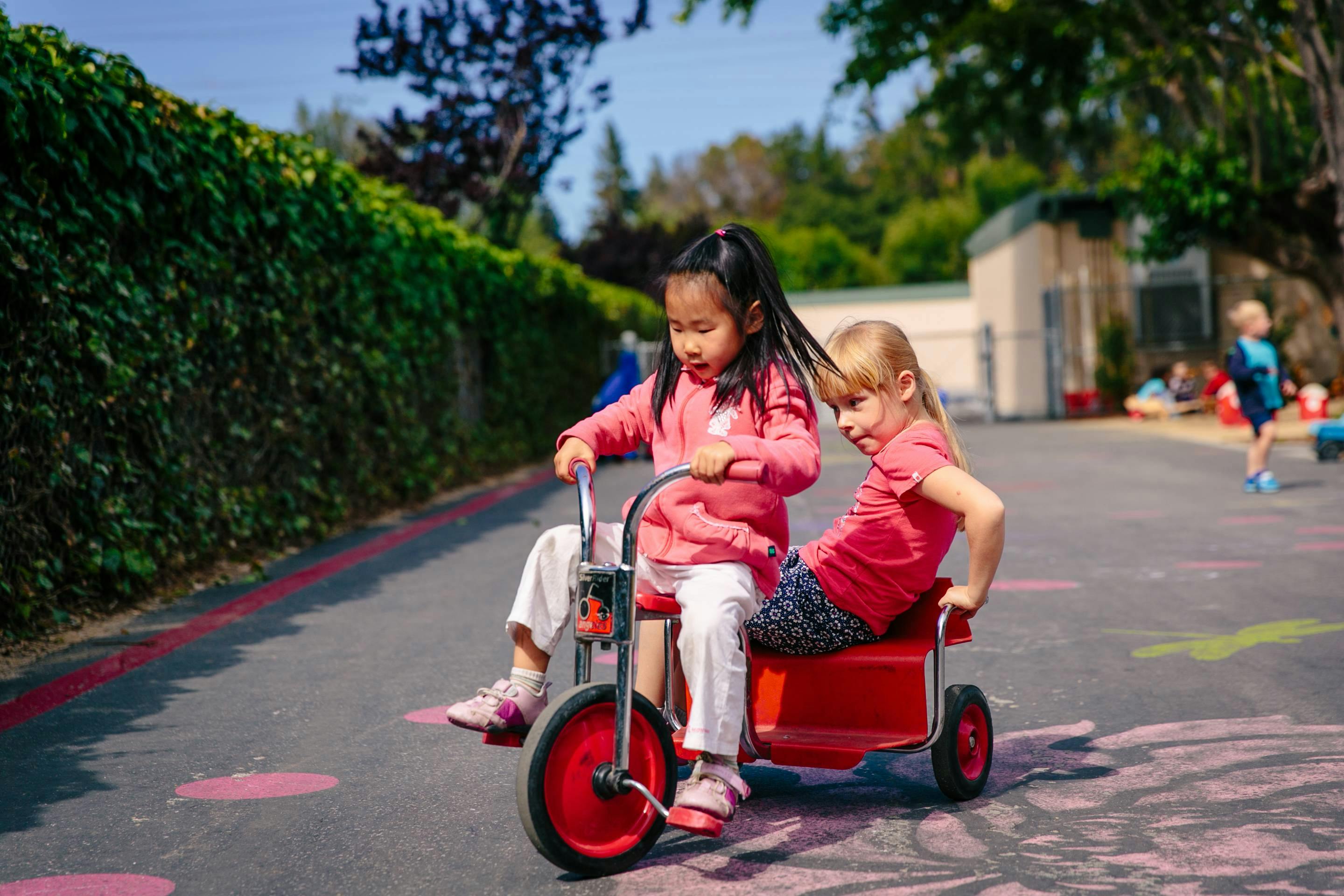 Two children riding a red tricycle together