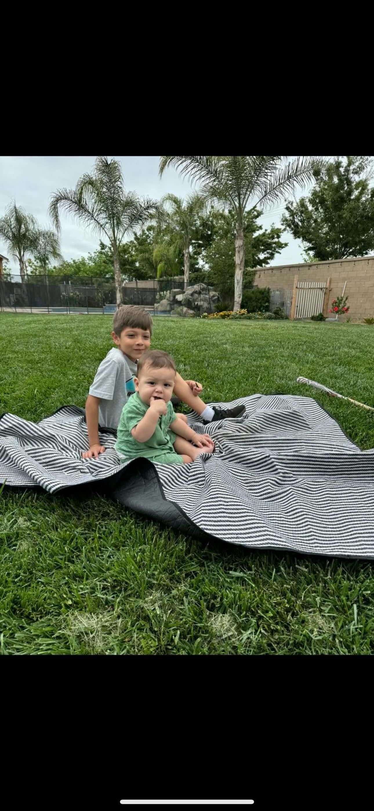 Two children sitting on a striped blanket on grass