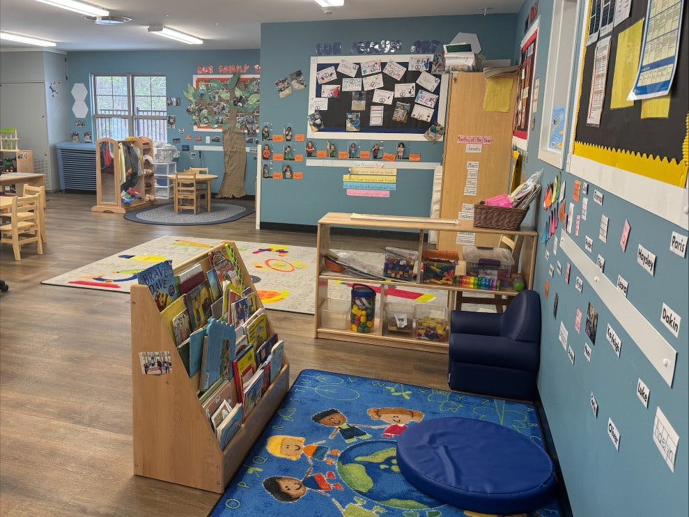 A classroom with a bookshelf, tables, chairs, and colorful rugs