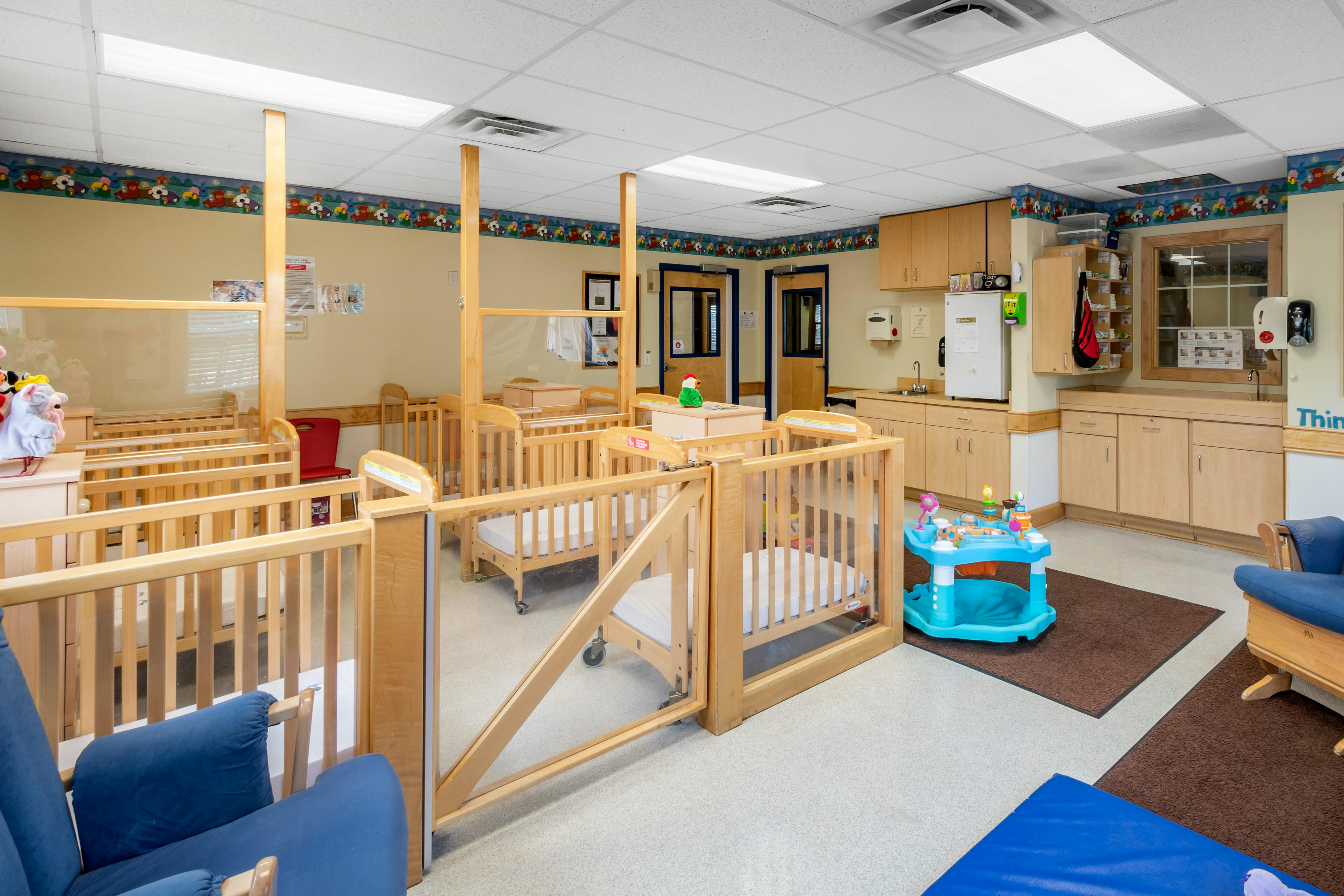 cribs in a daycare room with a changing station and sink area