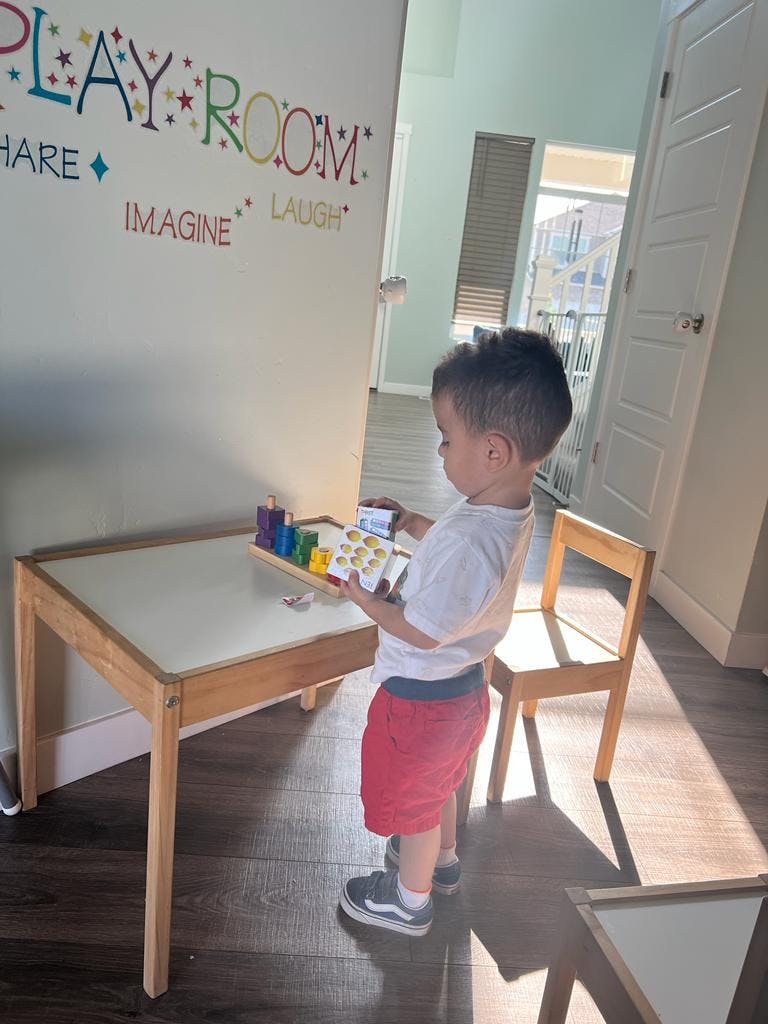 Child standing at a small table holding a toy with colorful blocks