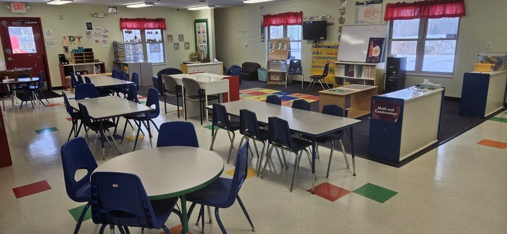 Empty classroom with multiple tables and chairs arranged, colorful floor tiles
