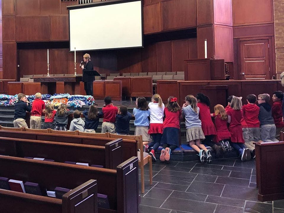 Children kneeling in front of a person speaking on a stage