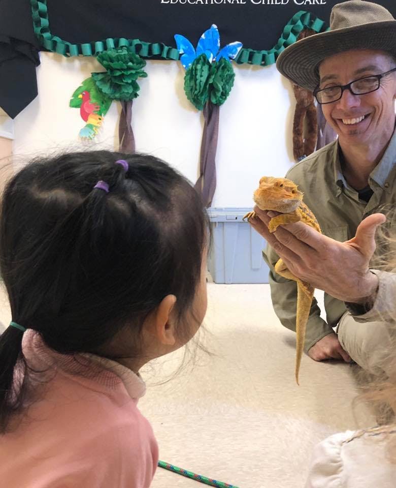 Person in hat holding a lizard for a child to see