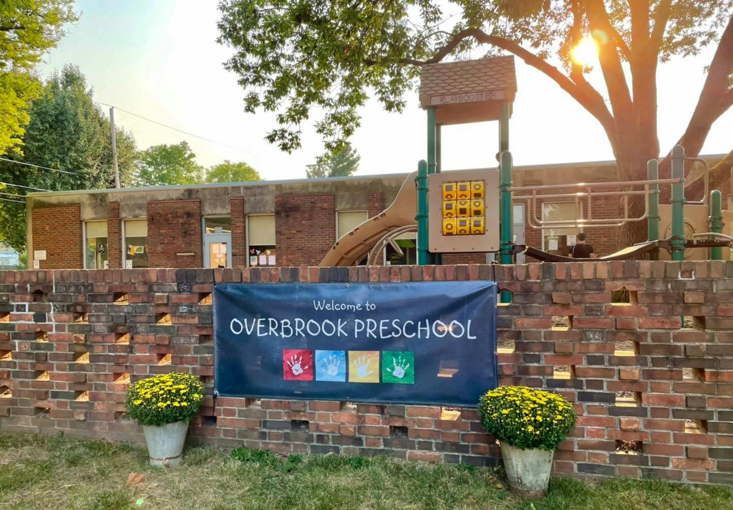 Welcome to Overbrook Preschool banner on a brick wall with a playground behind it the background