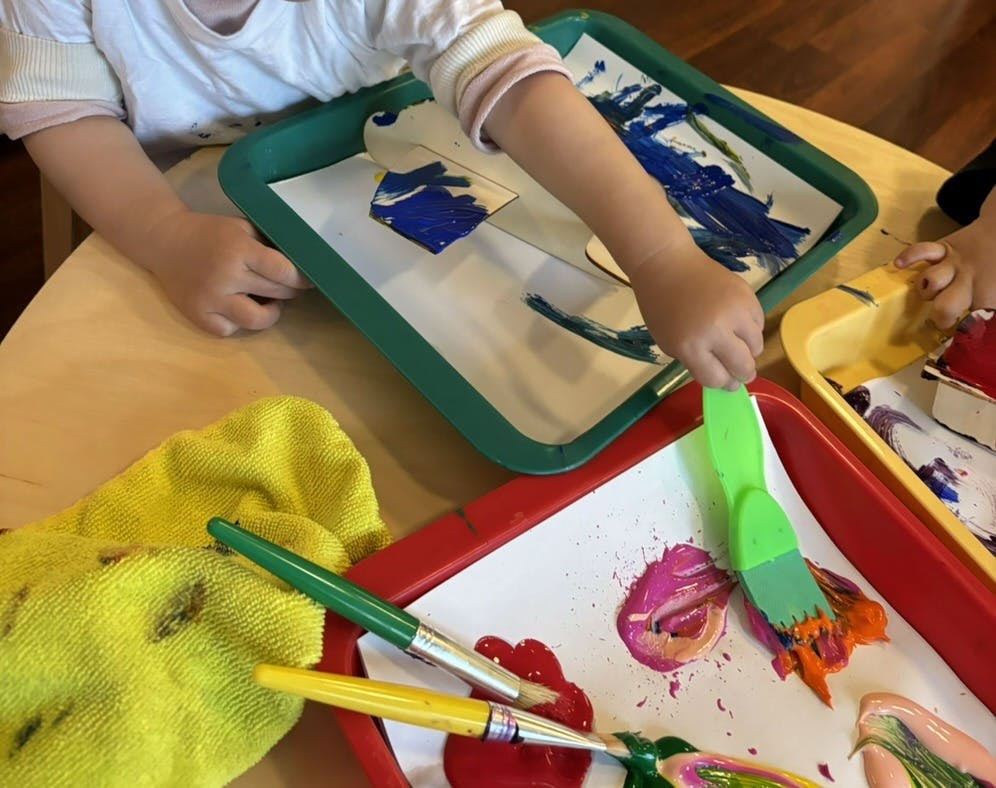 Child painting with a brush and mixing colors on a tray