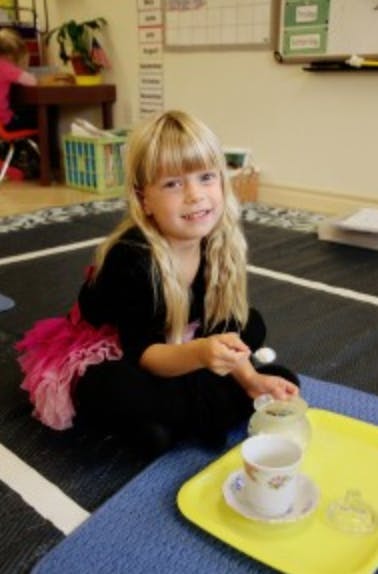 Child sitting on floor with a tea set on a yellow tray