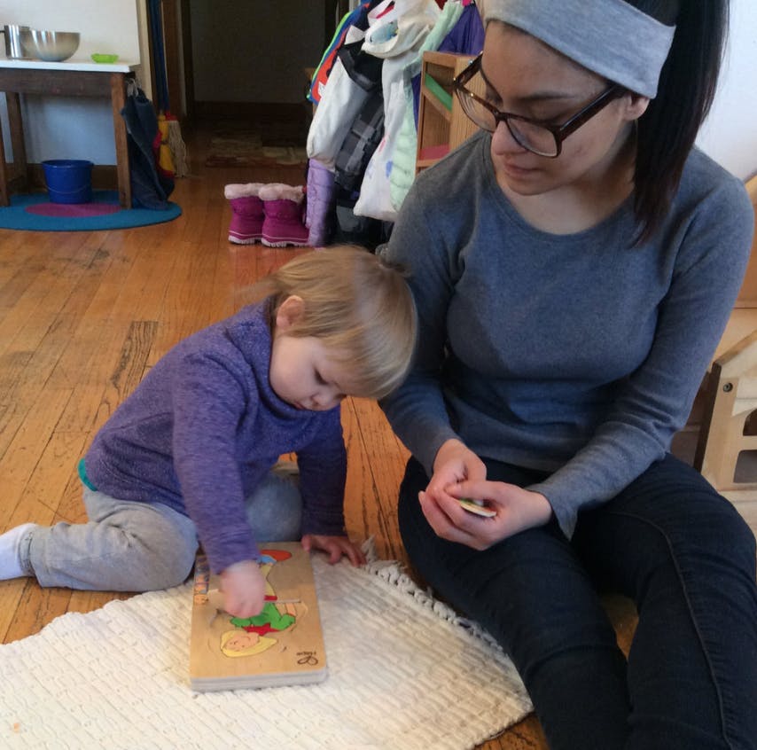 Person and child playing with a wooden puzzle on the floor
