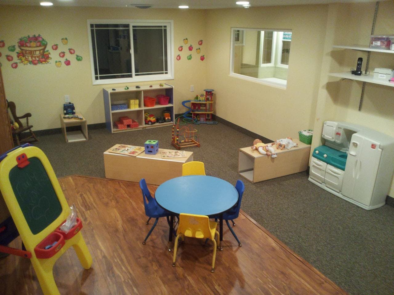 Playroom with small tables and chairs, shelves with toys, and an easel