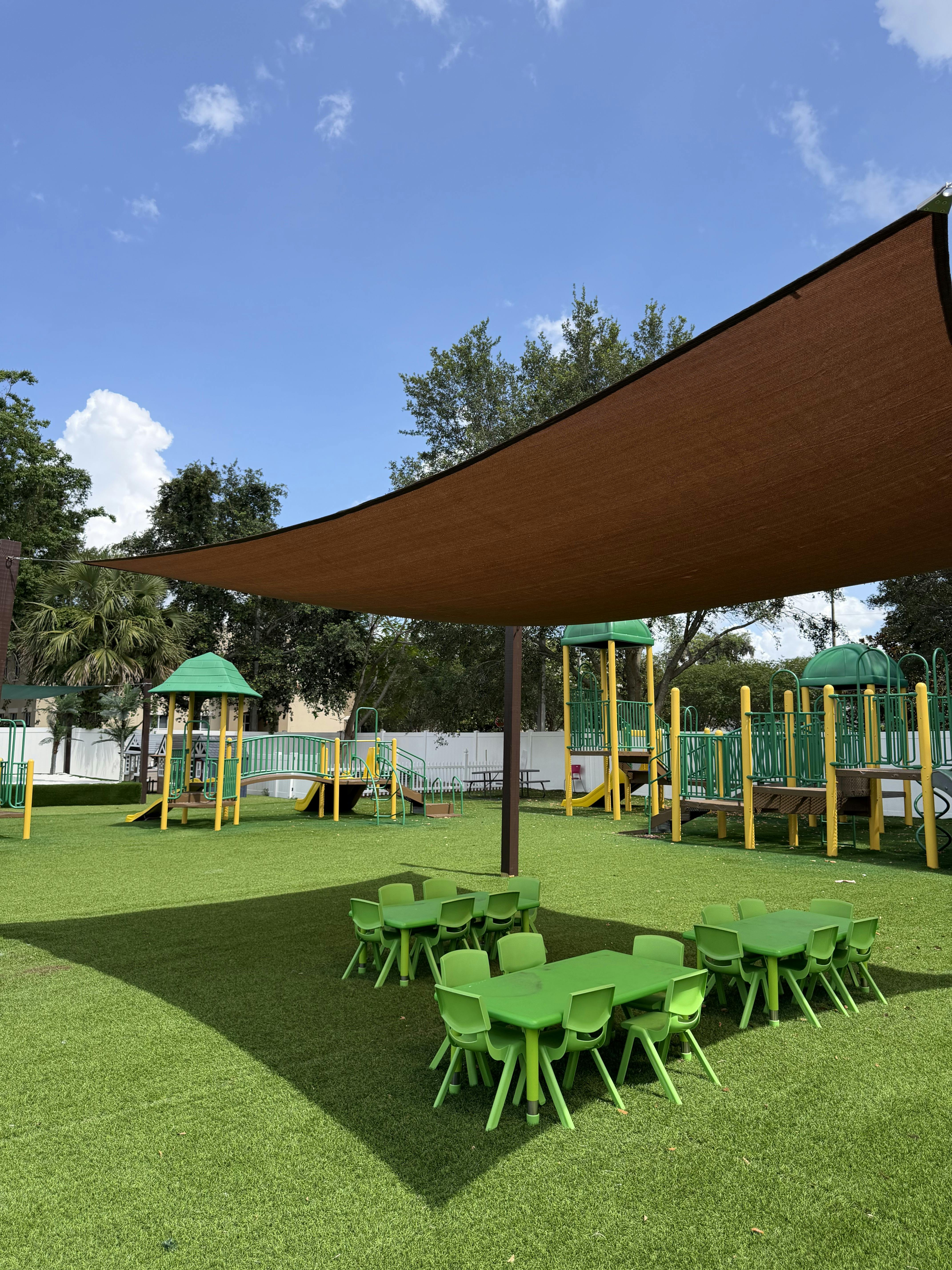 Small plastic tables and chairs on a playground under a large shade sail