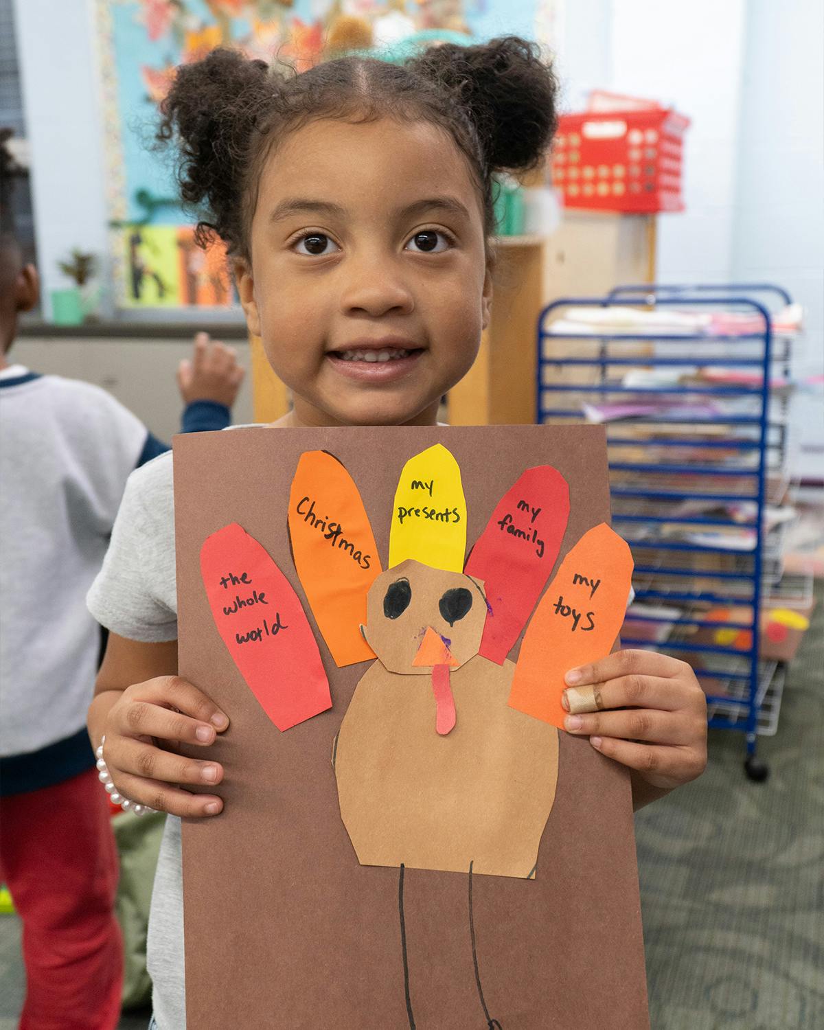 Child holding a turkey craft with text on feathers
