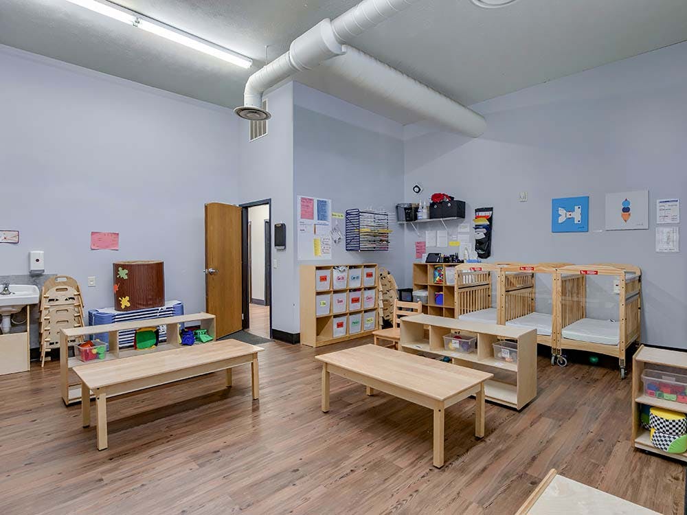 Classroom with cribs, small tables, and shelves of toys