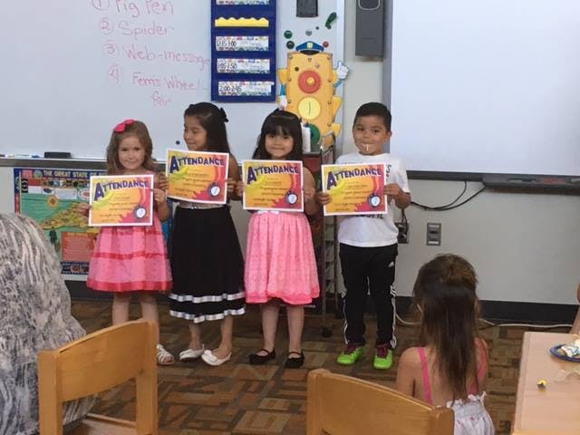 Four children holding up certificates in a classroom