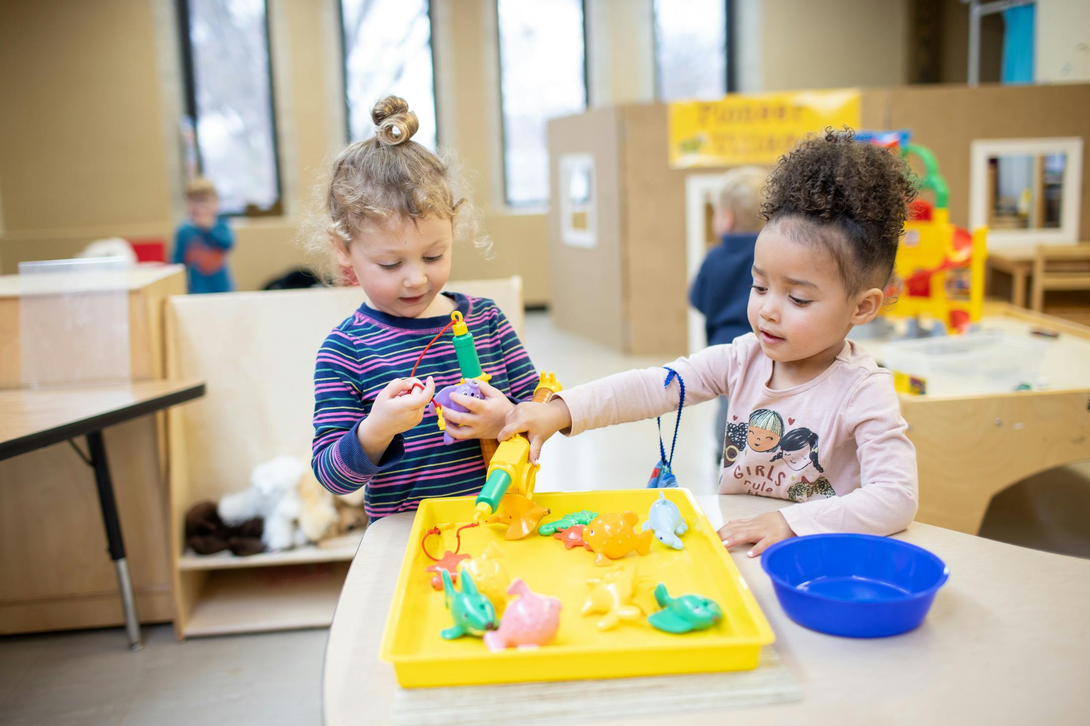 Two children playing with toys in a yellow tray