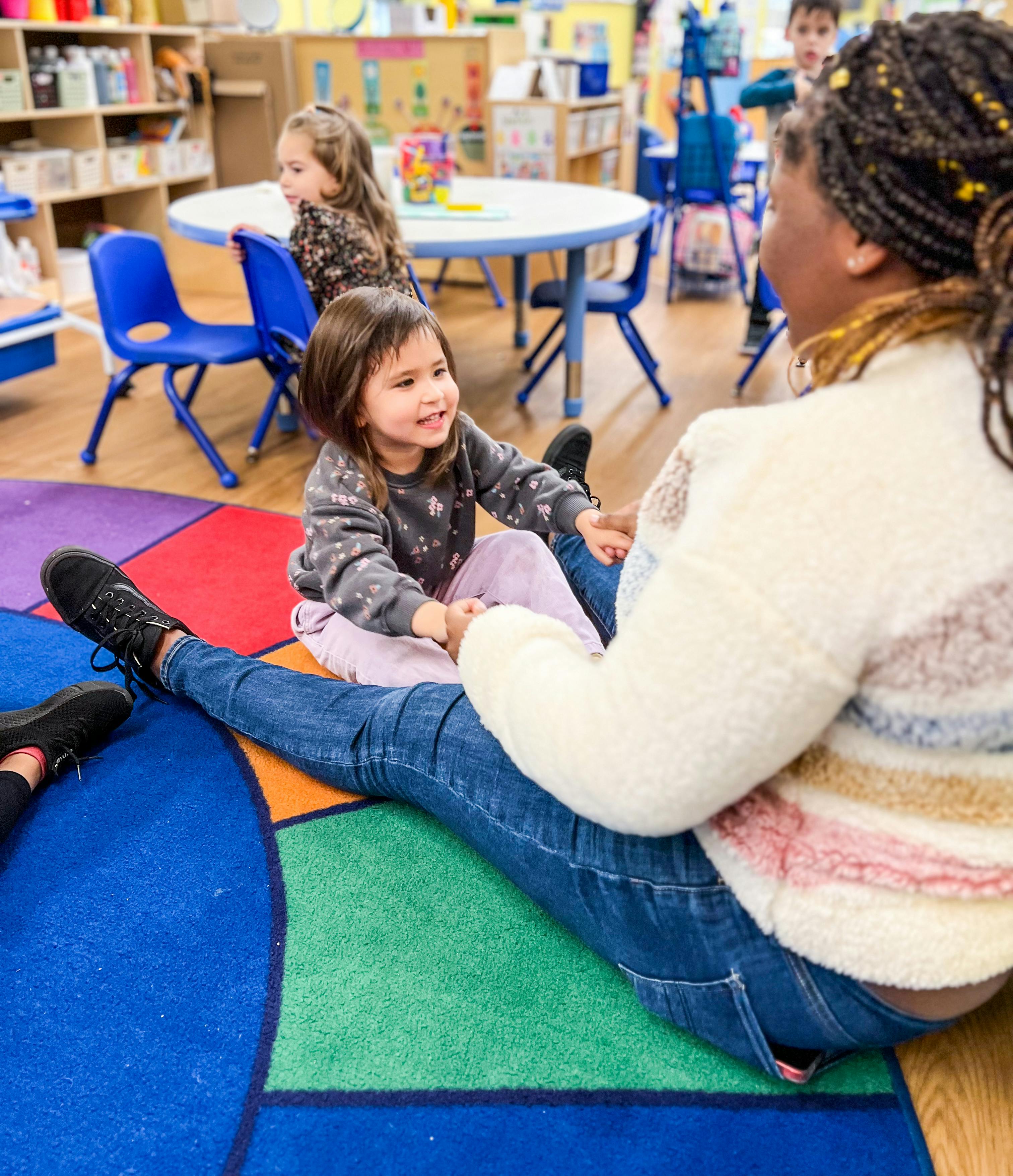 Adult and child sitting on a colorful rug in a classroom