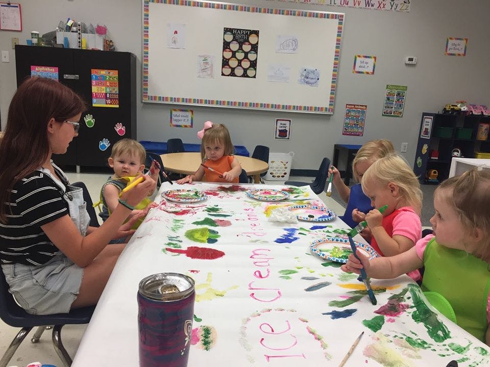 Person and children painting at a table in a classroom