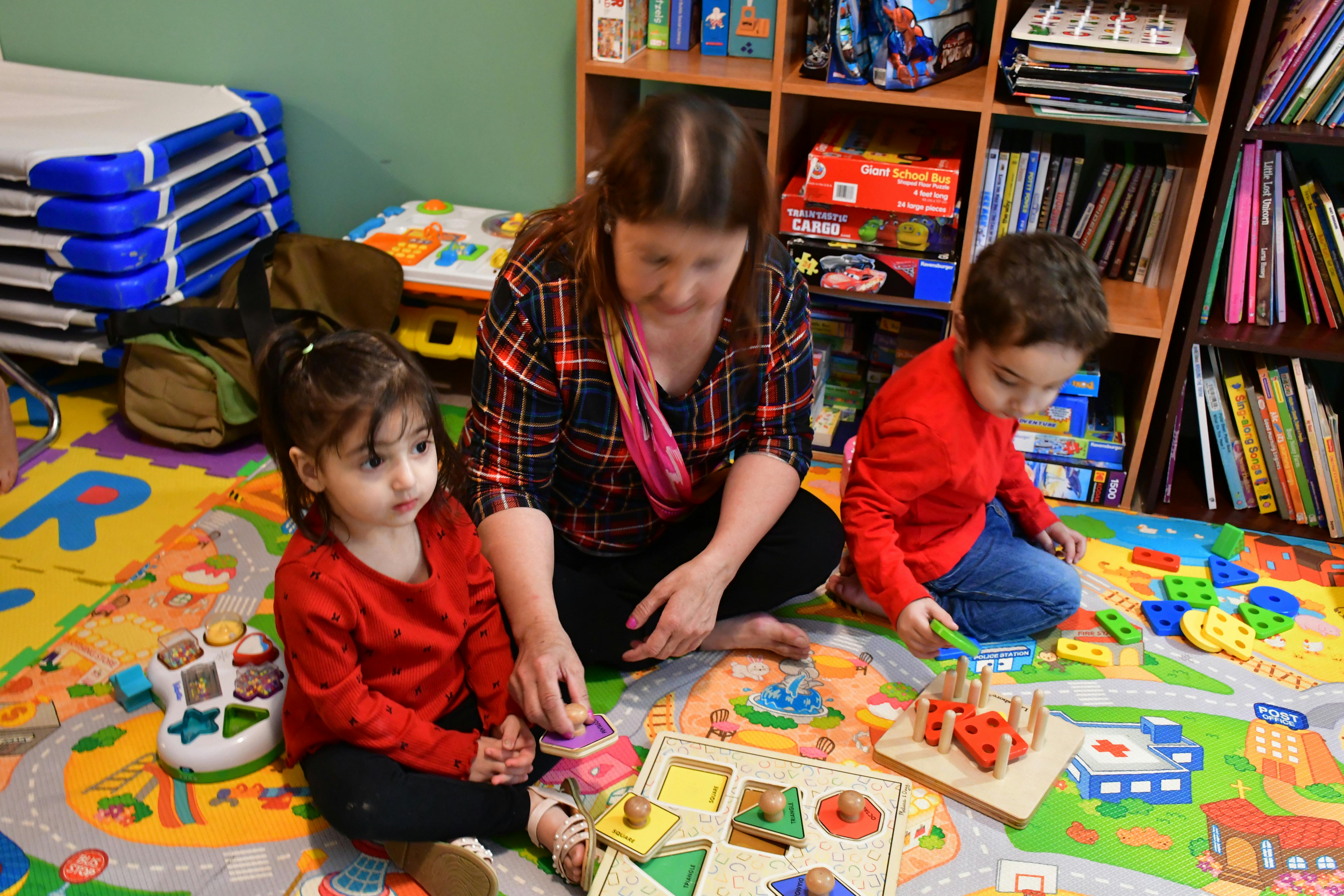 Person and two children playing with toys on a mat