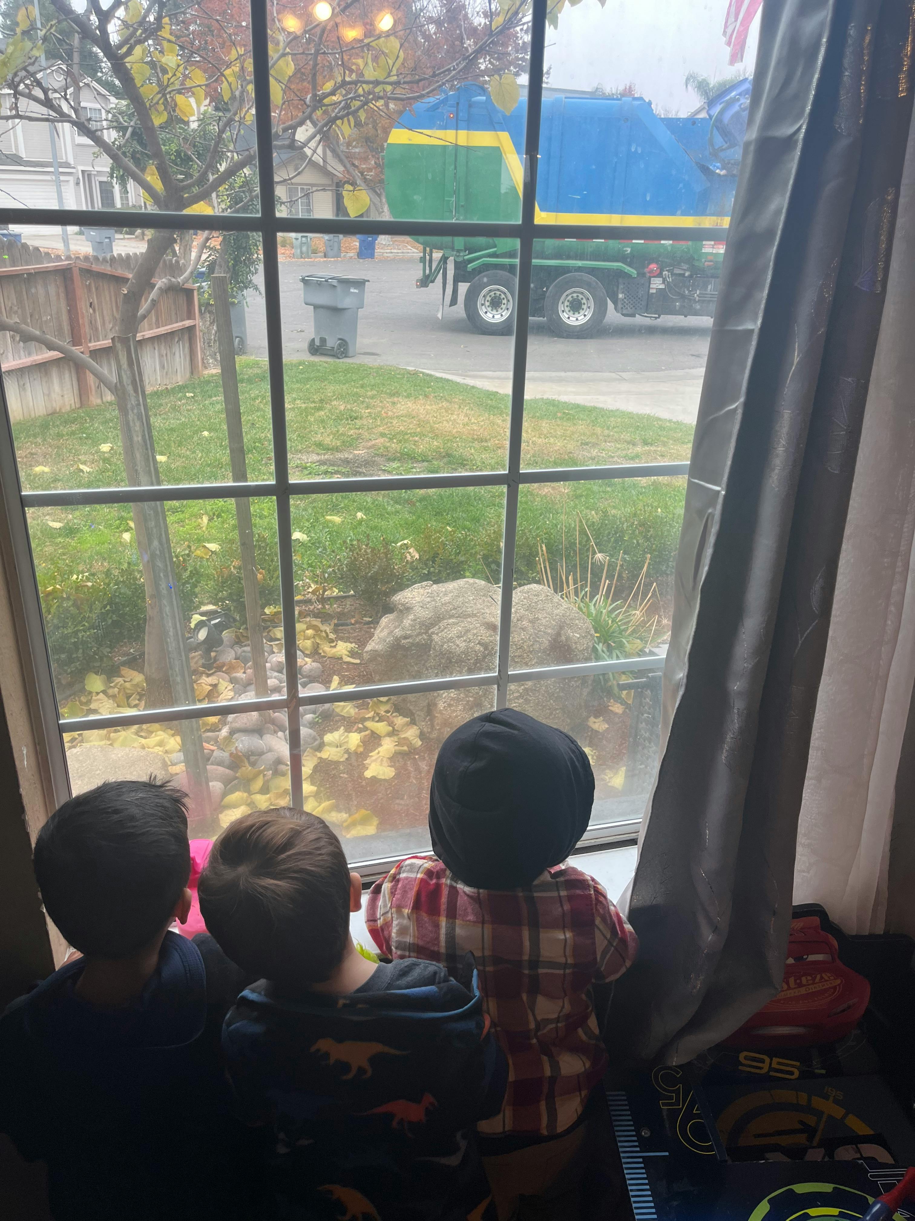 Three children looking out a window at a garbage truck