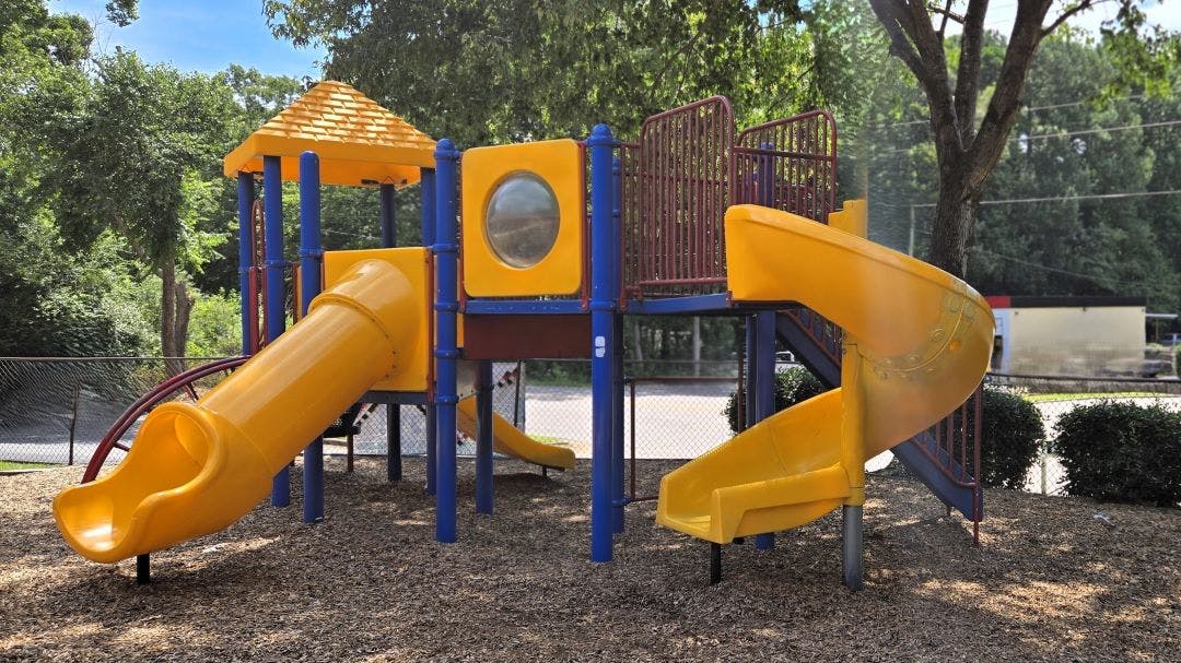 Yellow and blue playground structure with slides on wood chip ground