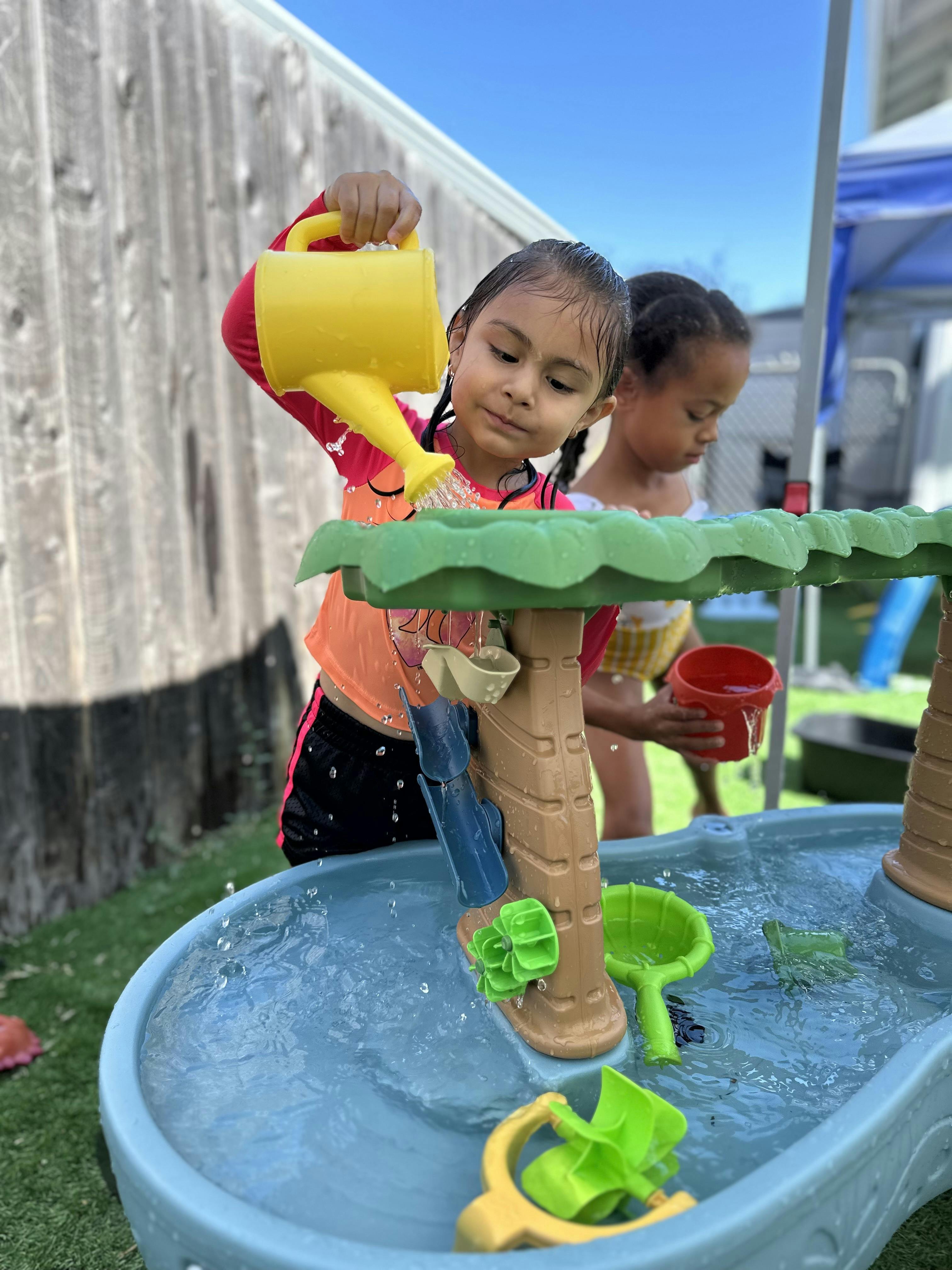 Two children playing with a water table in a backyard