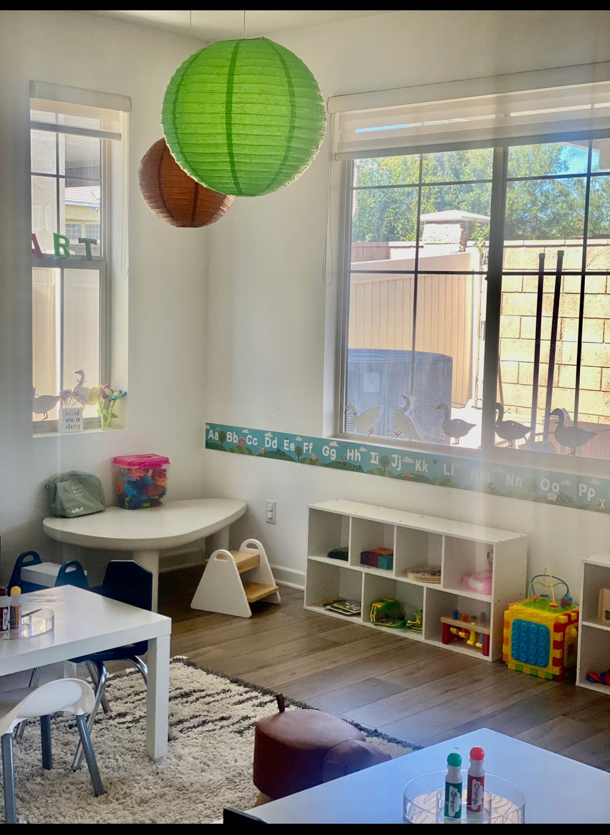 Children's classroom with small tables and chairs, white shelves, and ABC border