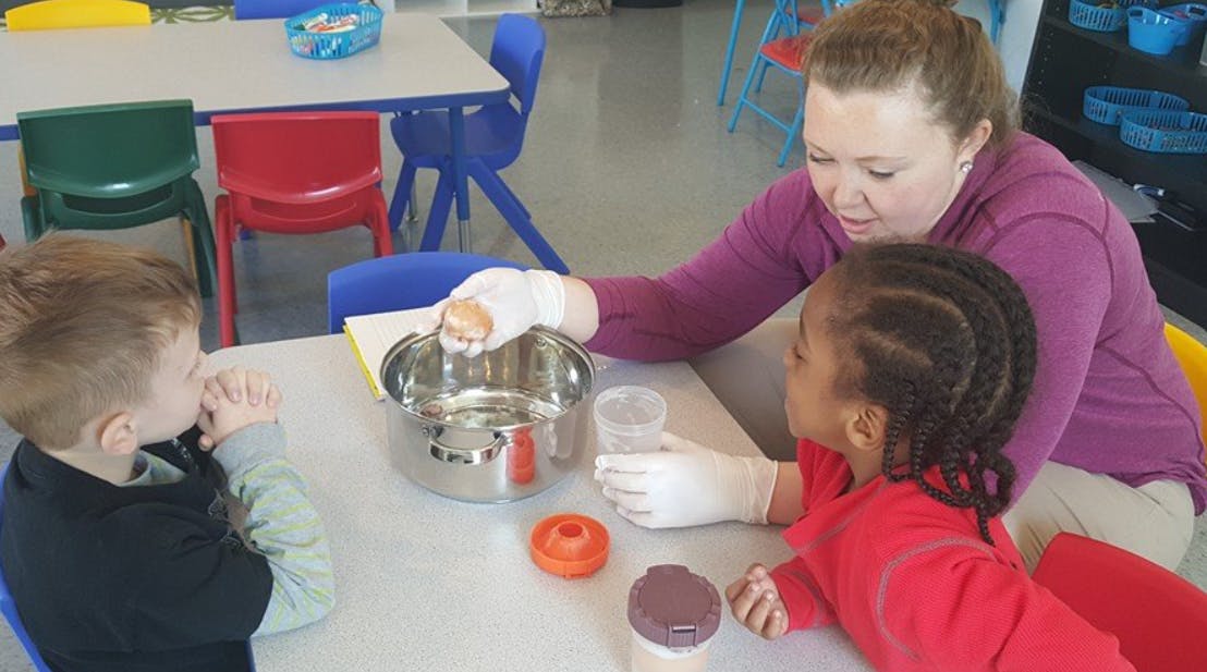Person and two children at a table with a pot and cups