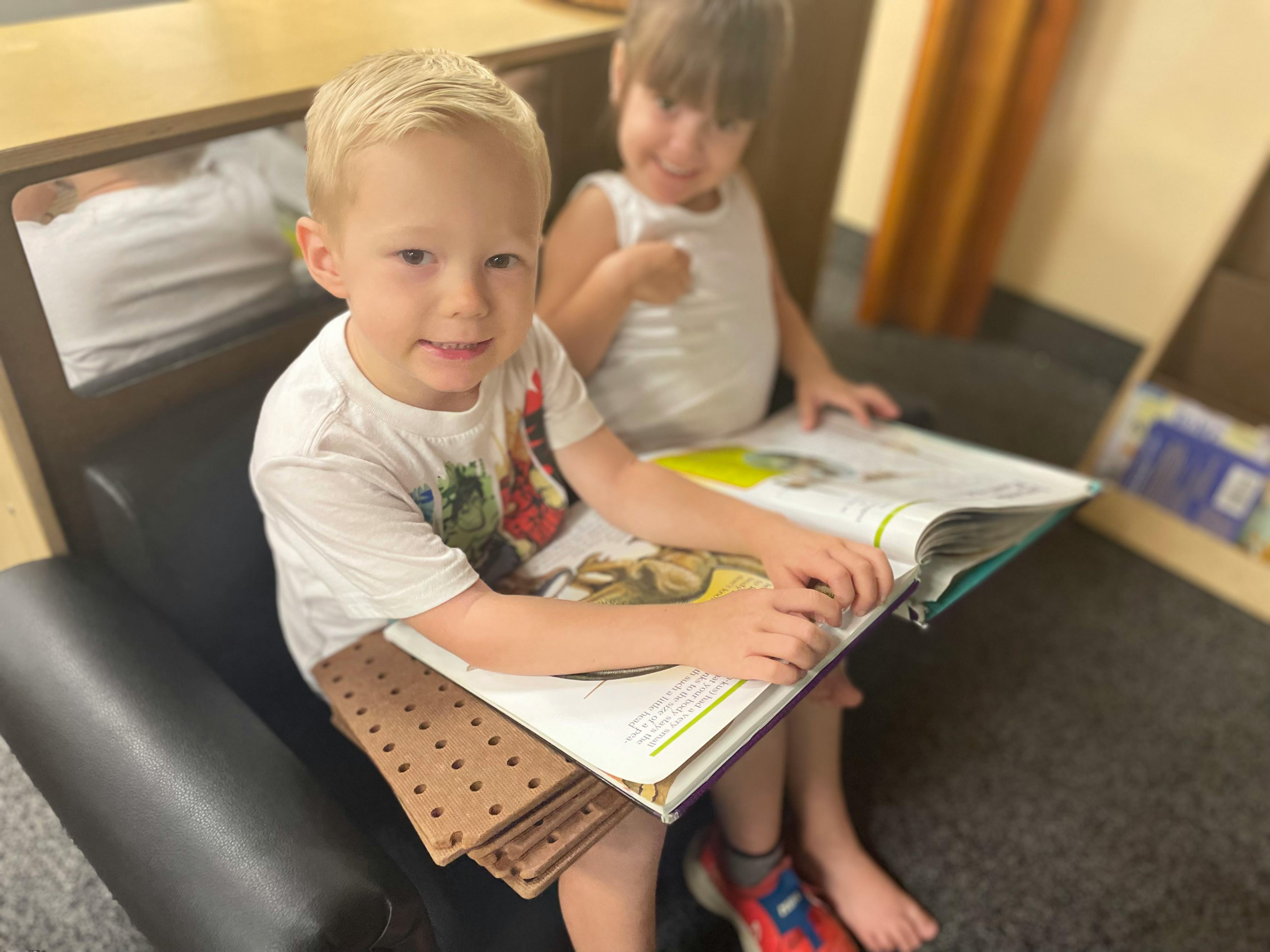 Two children sitting on a chair reading a book