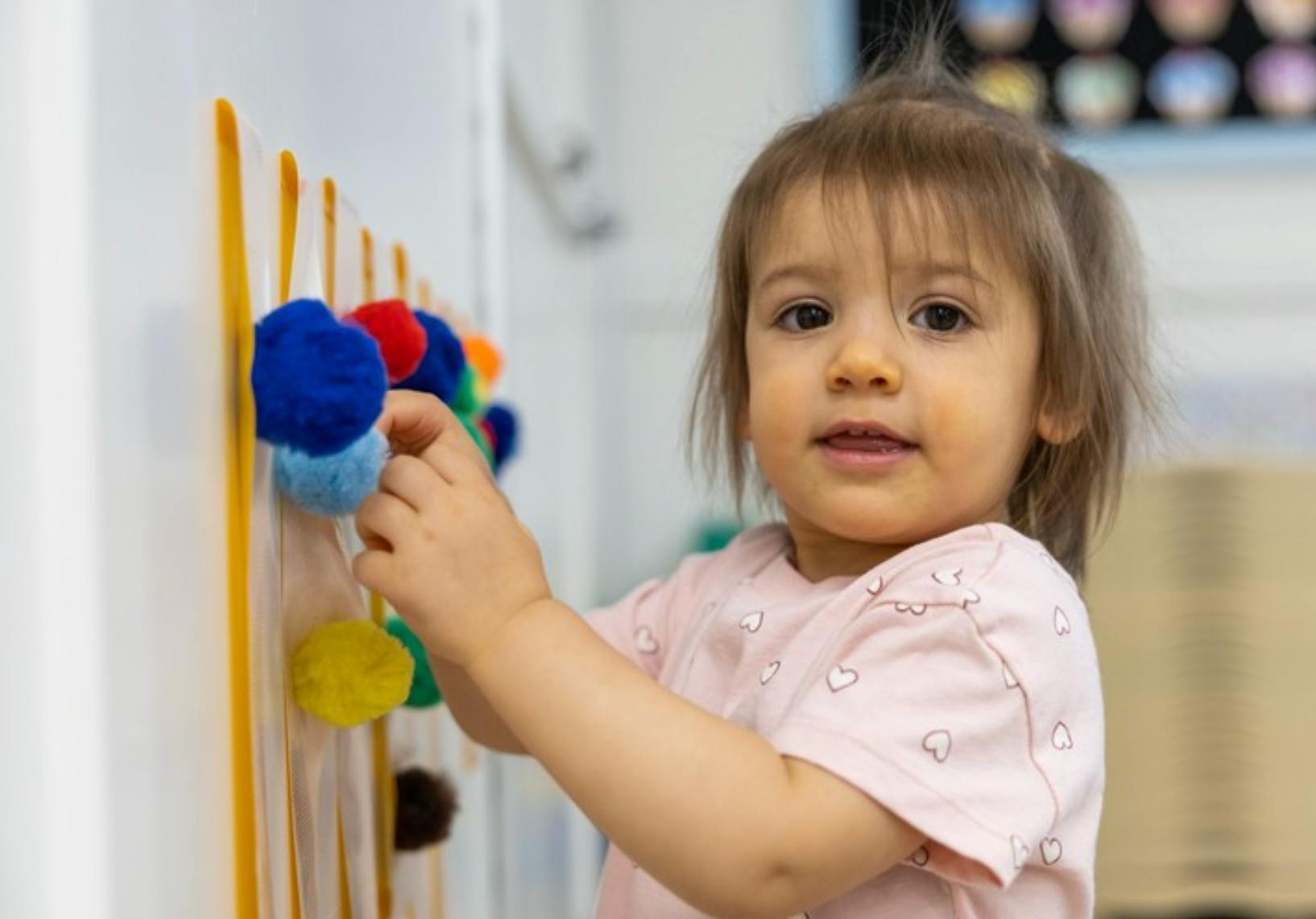 Child looking at camera while playing with colorful pompoms on a board