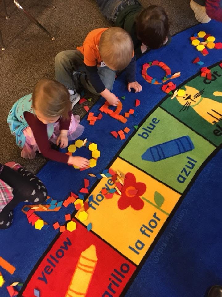 Children playing with colorful shapes on a rug with words and pictures