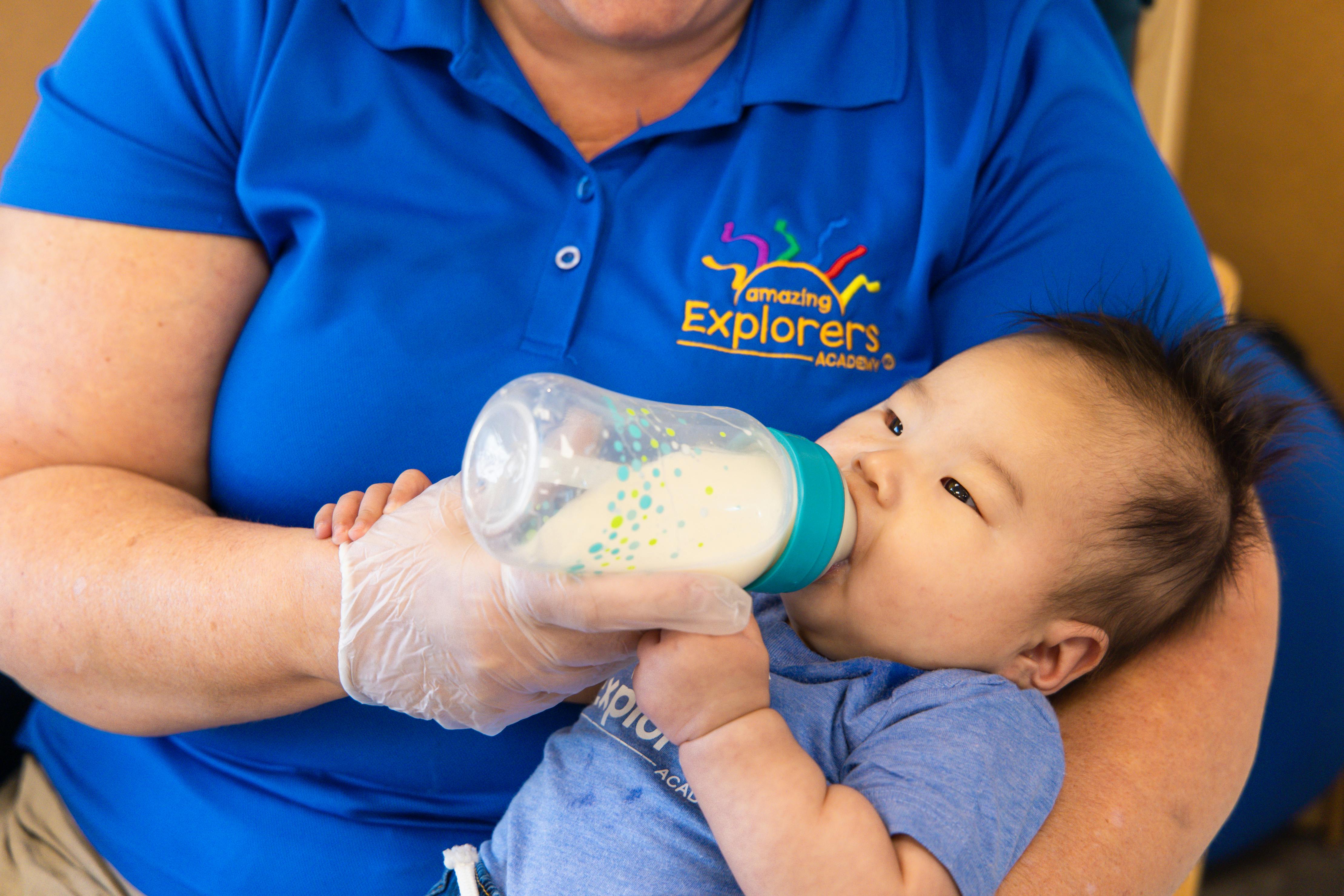 Person in blue shirt feeding a child with a bottle