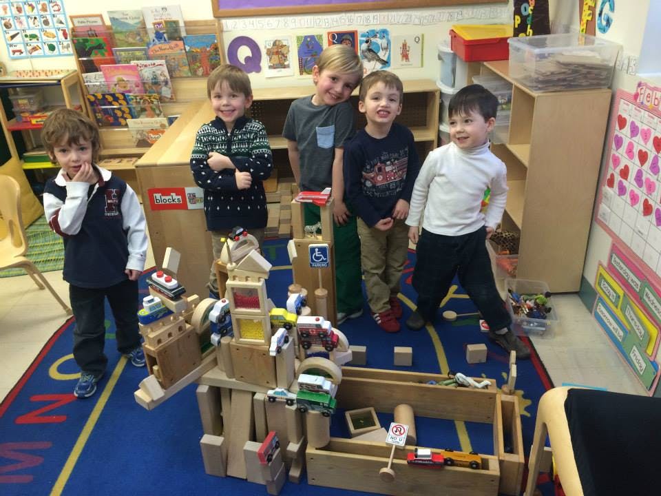 Five children standing around a large wooden block structure in a classroom