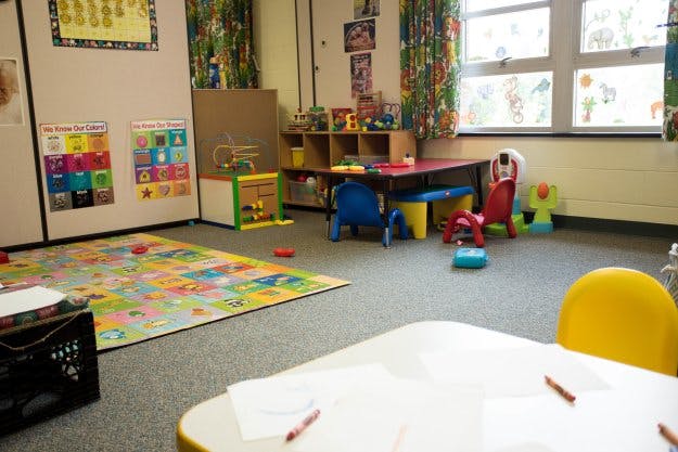 Empty classroom with small tables, chairs, and a colorful playmat
