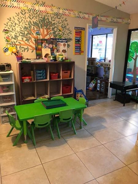 Classroom with a green table and chairs, shelves, and a tree mural on the wall