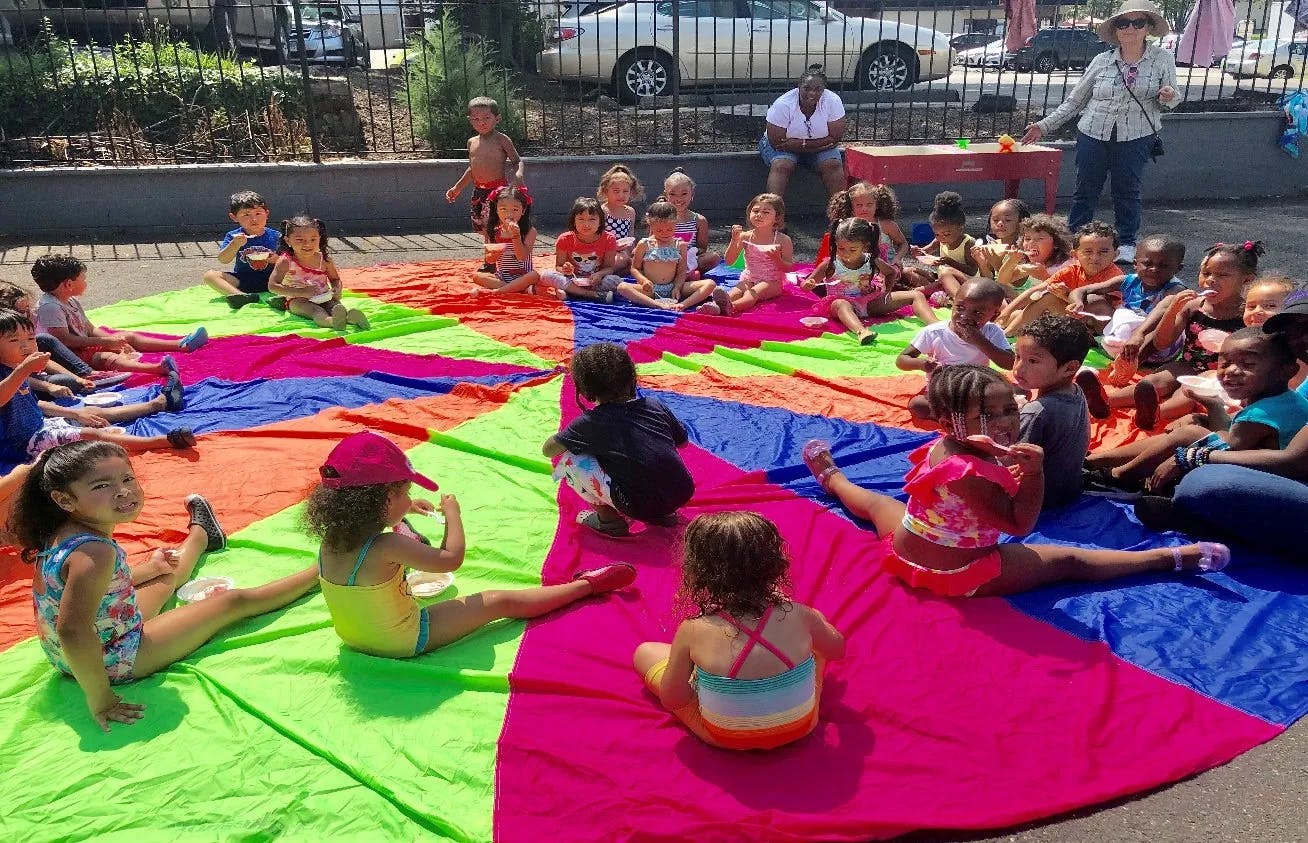 Many children sitting on a colorful parachute outdoors