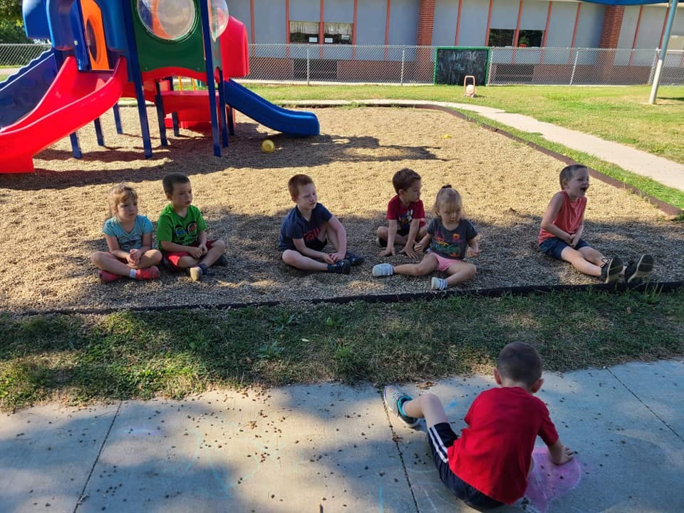 Children sitting on the ground near a playground
