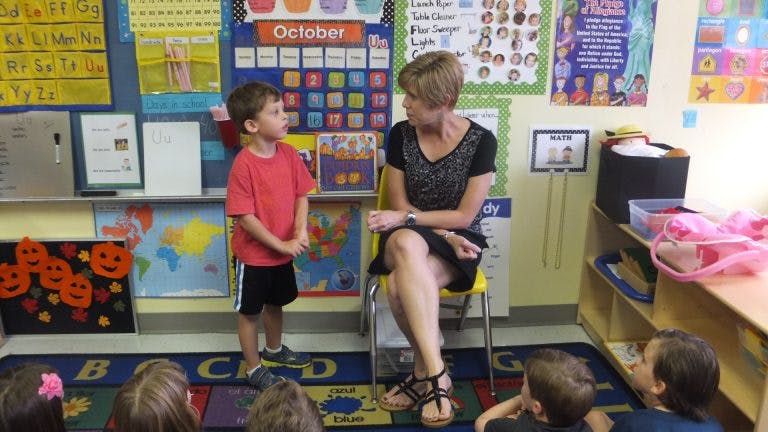 Adult and child talking in a classroom with other children on the floor