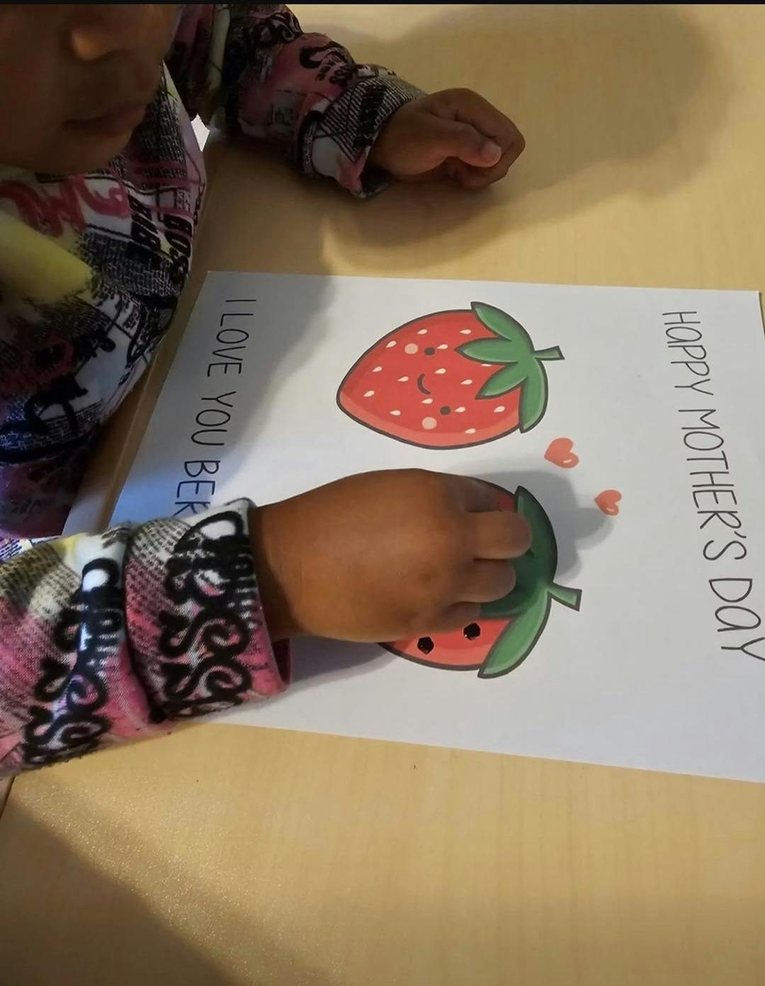 Child coloring a Mother's Day card with strawberry illustrations