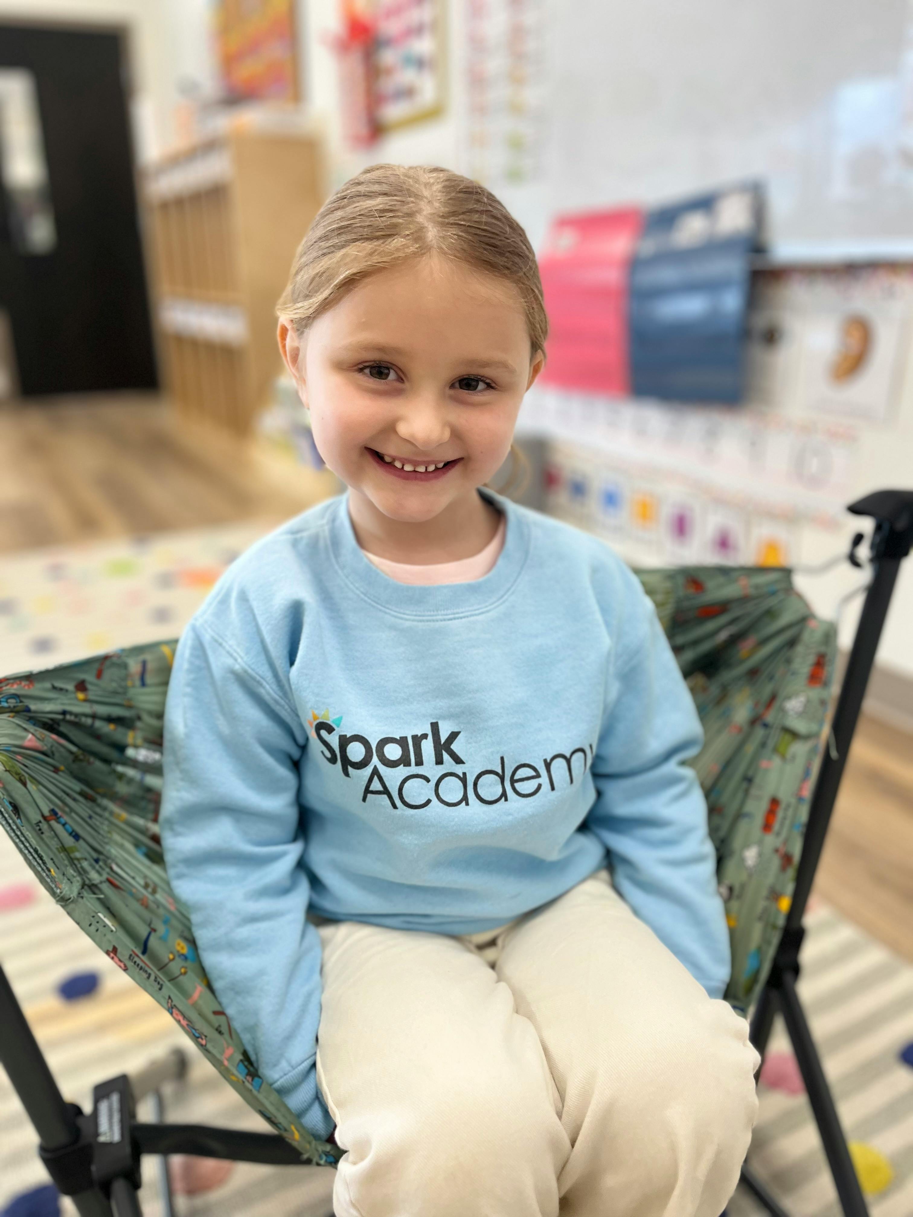 Child in a light blue Spark Academy sweatshirt, seated in a classroom