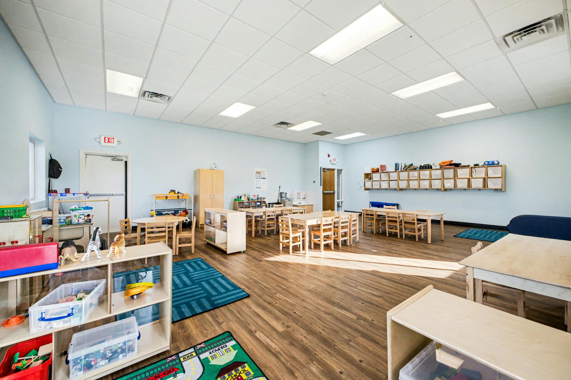 Empty classroom with small tables and chairs, shelves, and play mats