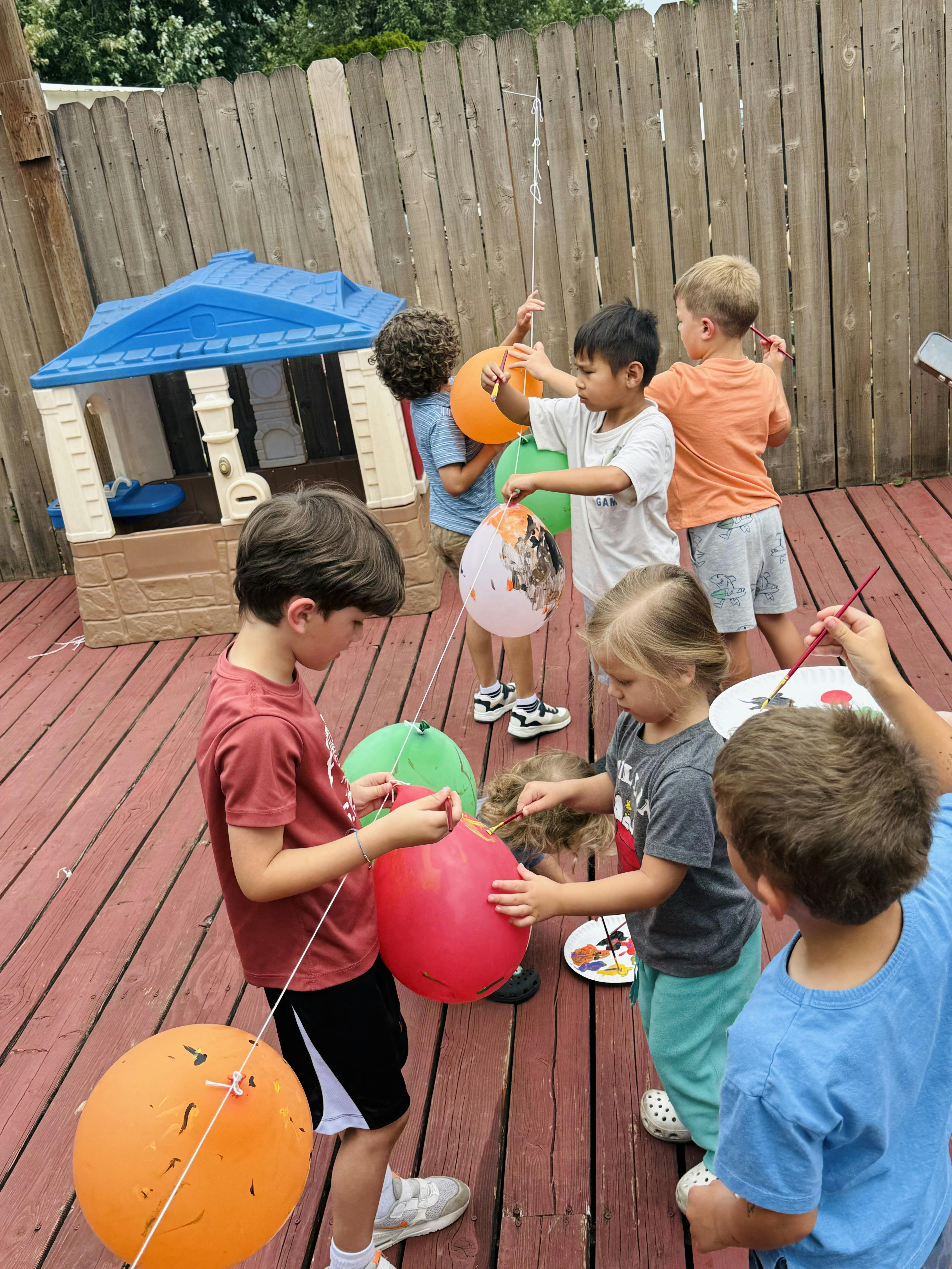 Group of children painting balloons on a wooden deck