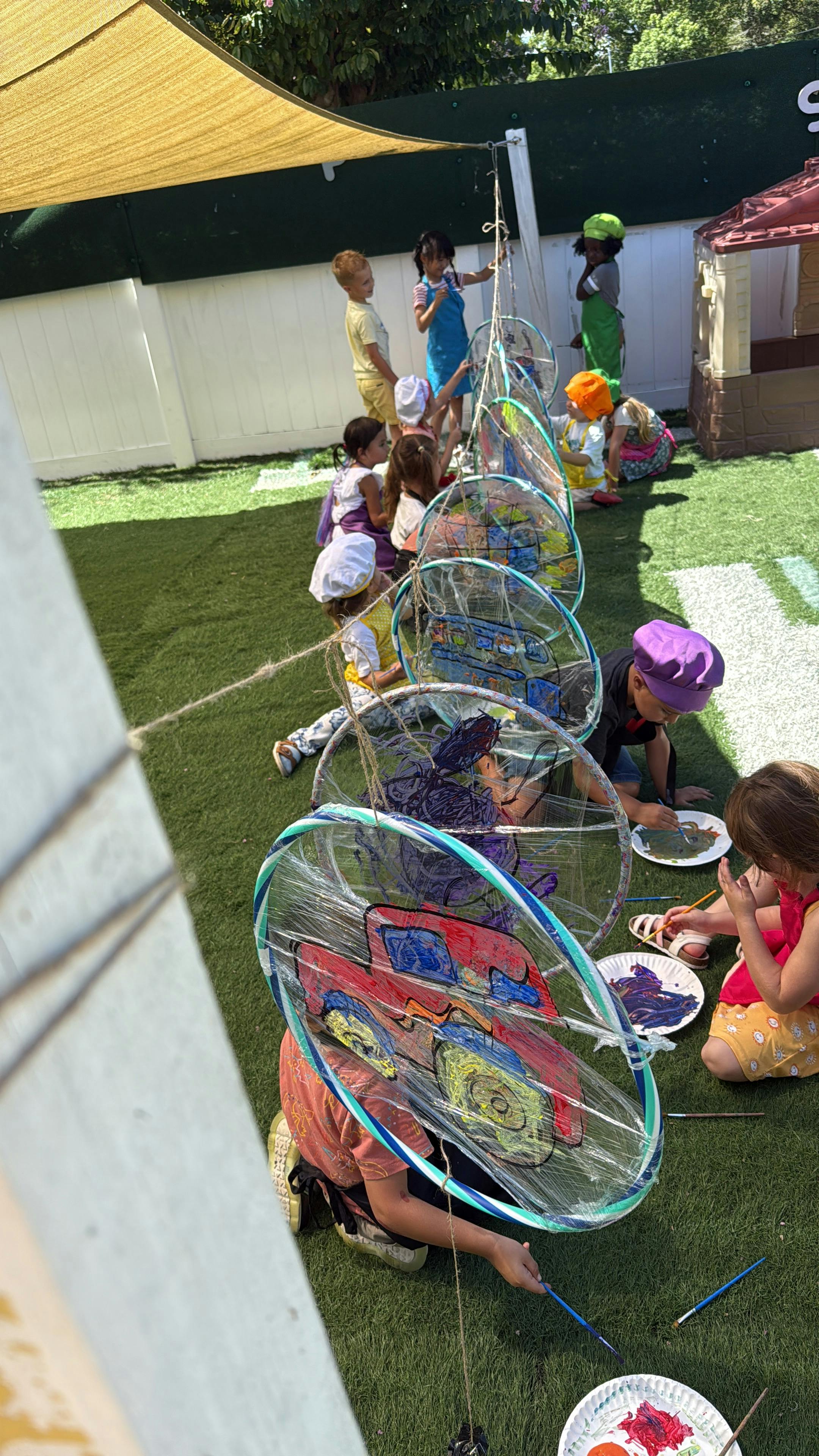 Children painting on clear circular canvases outdoors