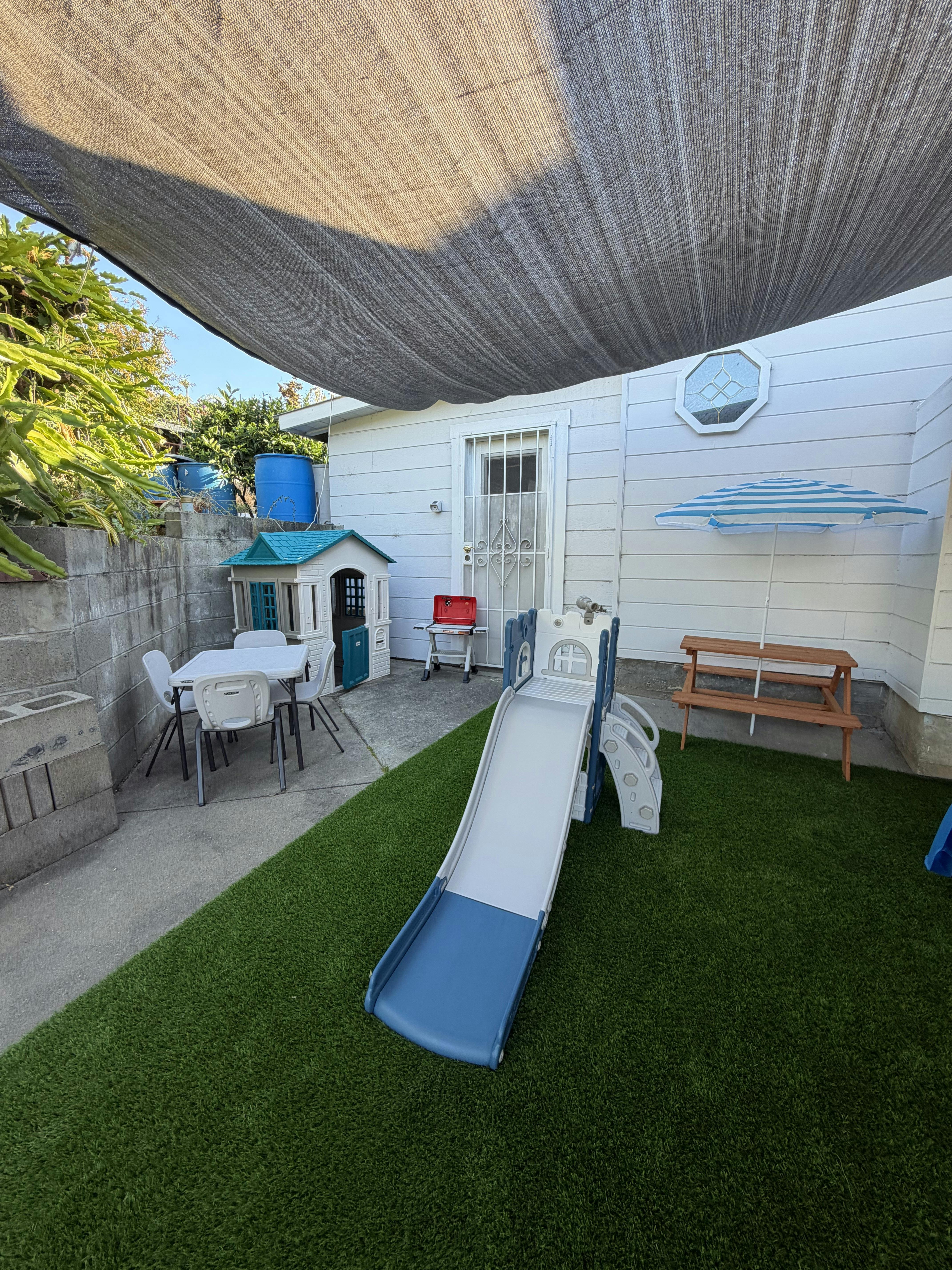 Play equipment and children's furniture in a backyard under a shade cloth